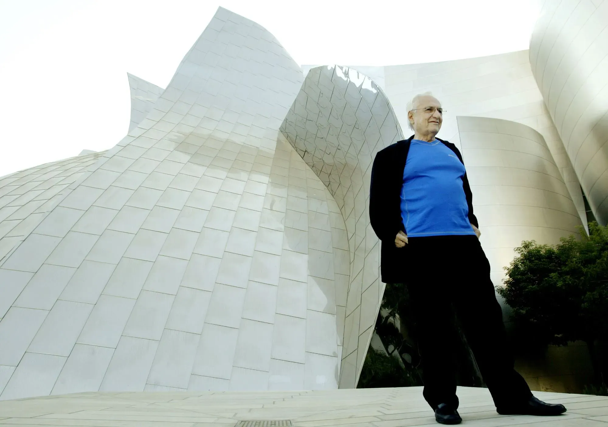 فرانك جيري يقف أمام تصميمه المعماري المبتكر، معالم متحف غوغنهايم، الذي يعكس رؤيته الفريدة في الهندسة المعمارية.