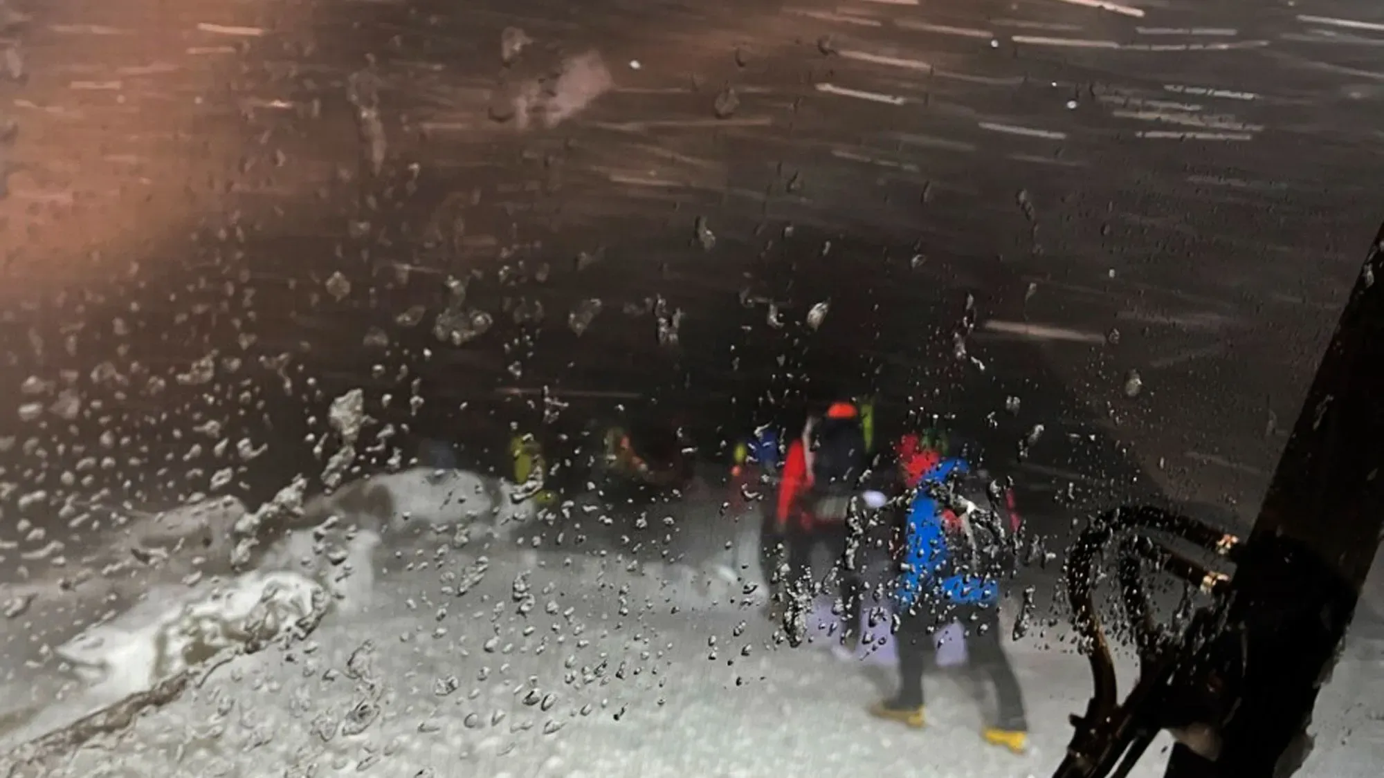 رجال إنقاذ يرتدون ملابس ملونة في ظروف ثلجية قاسية، يظهرون من خلال زجاج مبلل، أثناء محاولة إنقاذ متسلقين عالقين في جبل واشنطن.