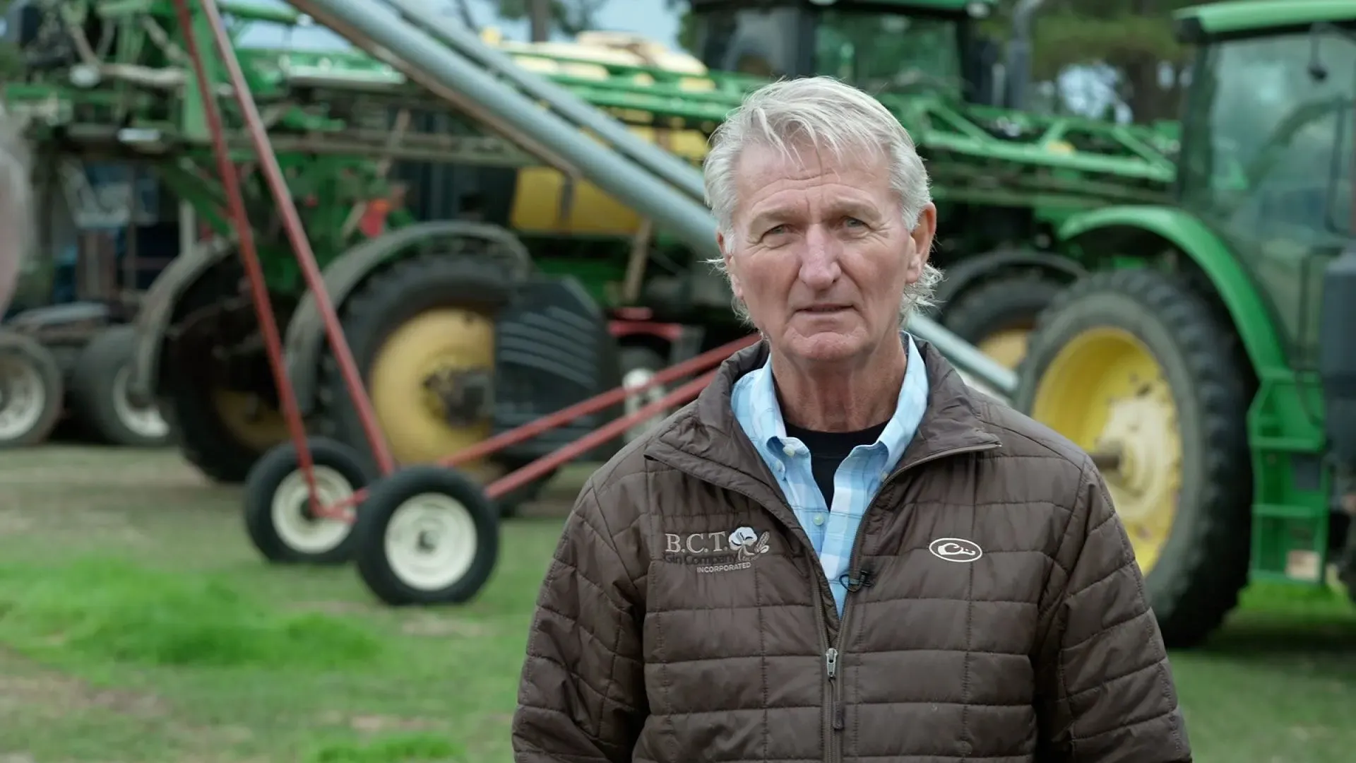 مزارع في جورجيا يقف أمام جرارات زراعية، معبرًا عن قلقه بشأن تأثير السياسات الاقتصادية على الزراعة.