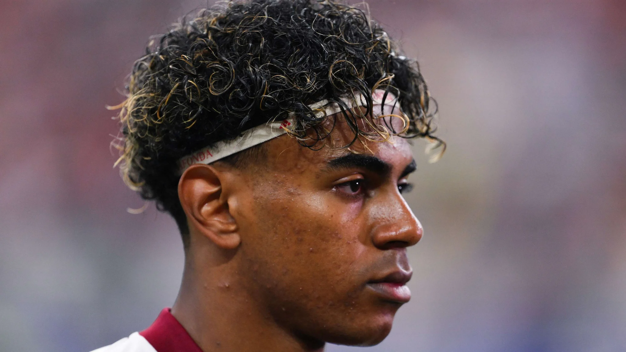 شاب يامال لاعب برشلونة والمنتخب الإسباني يركز بتركيز عالي خلال مباراة كأس العالم 2026، مع تسريحة شعر مميزة وخلفية ضبابية.