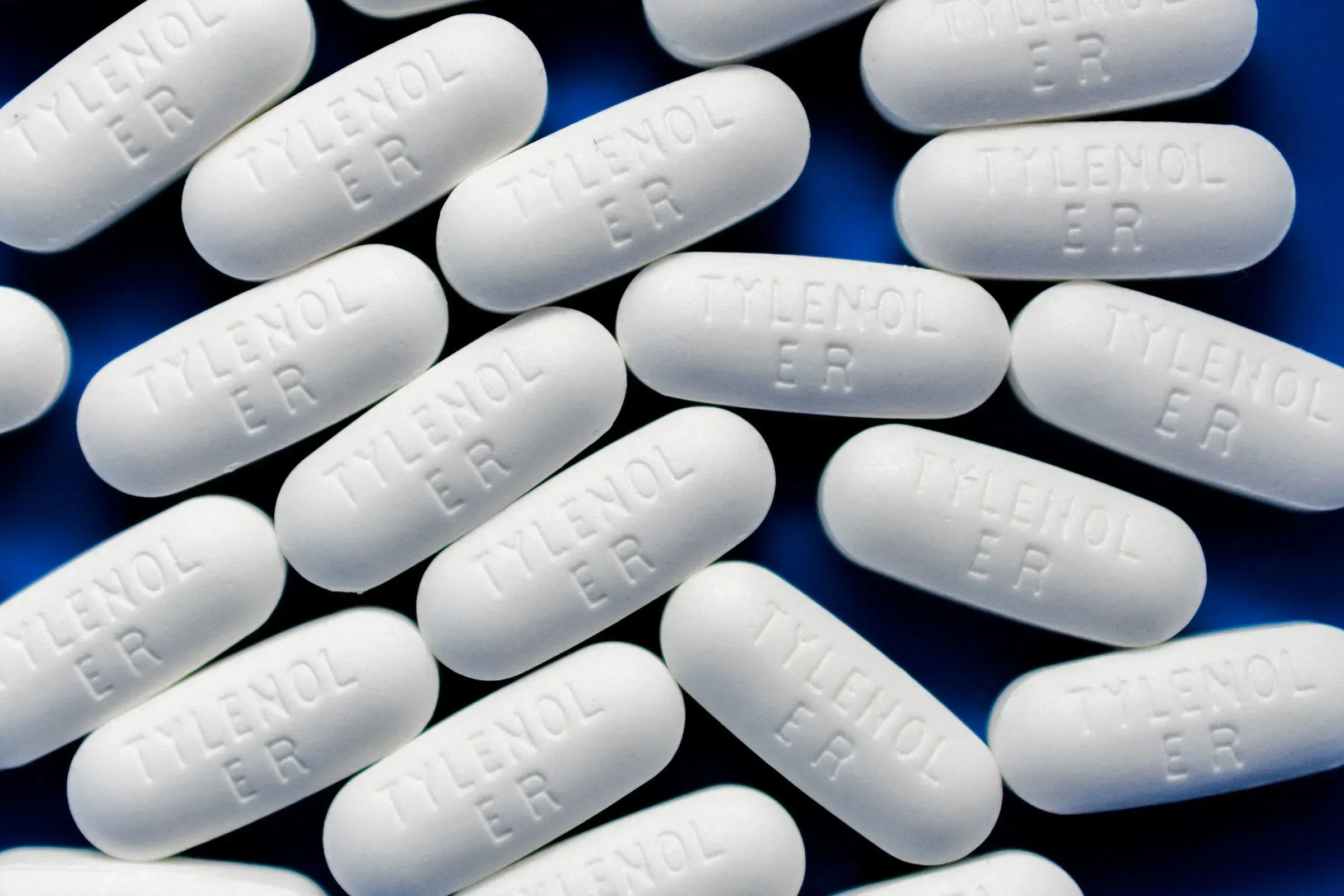 أقراص تايلينول البيضاء مرصوصة بشكل عشوائي على خلفية زرقاء، مما يعكس الجدل حول تأثيراتها على النساء الحوامل.