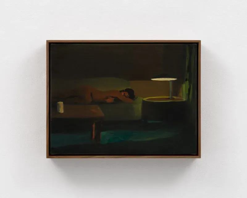 امرأة عارية تستلقي على أريكة في غرفة مضاءة بشكل خافت، مع طاولة بجانبها ومصباح يضيء المكان، تعكس لحظة من الاسترخاء والعزلة.