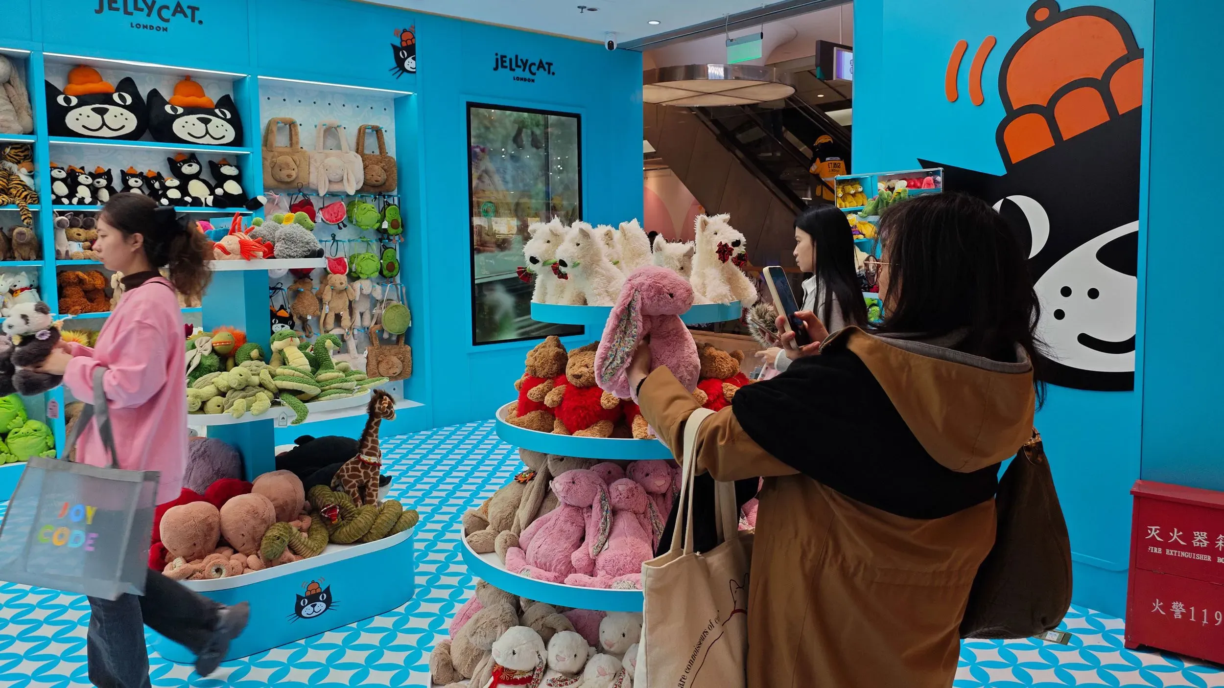 متجر دمى محشوة يعرض مجموعة متنوعة من دمى Jellycat الملونة، بينما تتجول زبائن بين الرفوف.