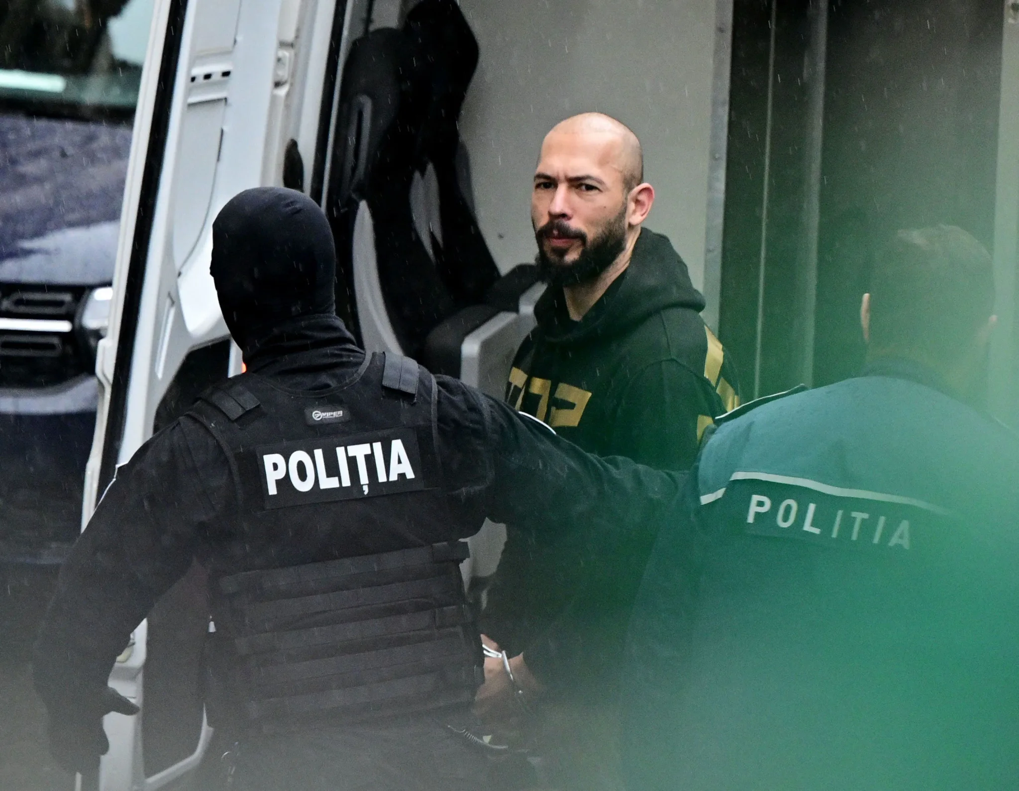 شاب يُعتقل من قبل شرطيين رومانيين يرتديان زي الشرطة خلال تنفيذ أمر اعتقال في رومانيا، مرتبط بقضية الأخوين Tate المثيرة للجدل.
