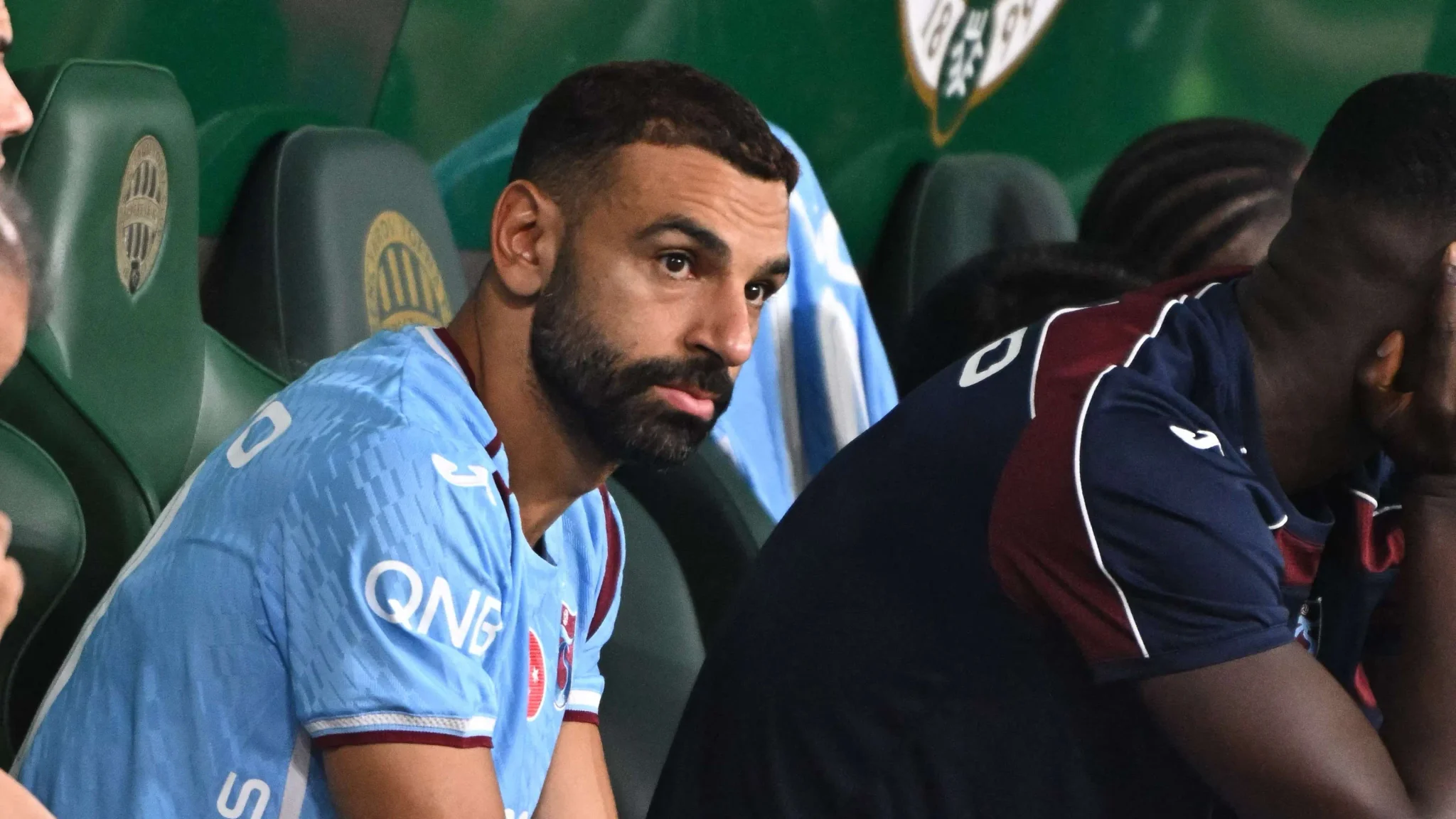 محمد صلاح جالس على مقاعد البدلاء خلال مباراة في دوري روشن السعودي، مع التركيز على تحديات صفقات الانتقالات الصيفية الكبرى.