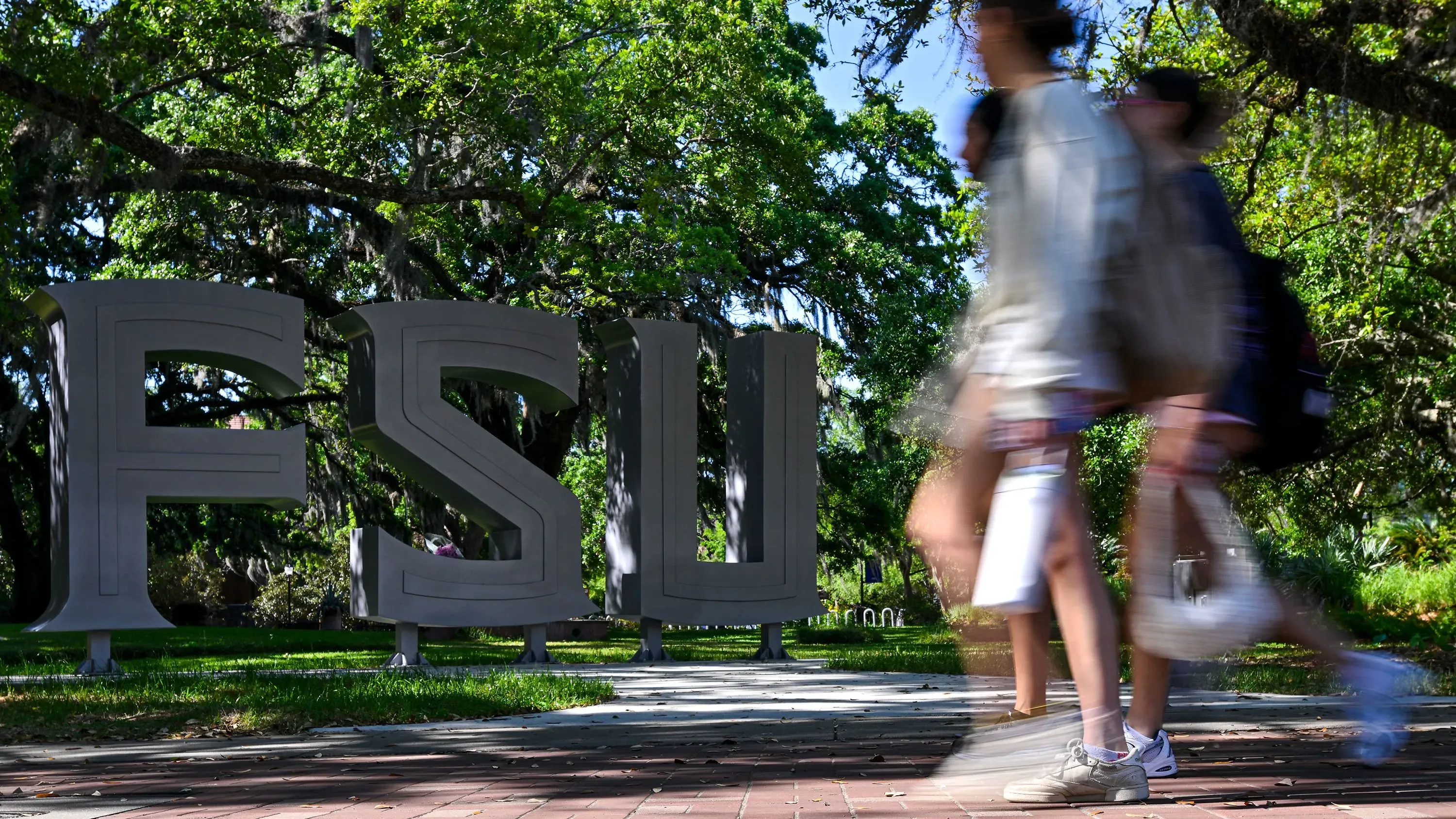 طلاب يمشون بجوار شعار جامعة ولاية فلوريدا (FSU) وسط أشجار خضراء، في ظل أجواء من الحزن بعد حادث إطلاق النار.