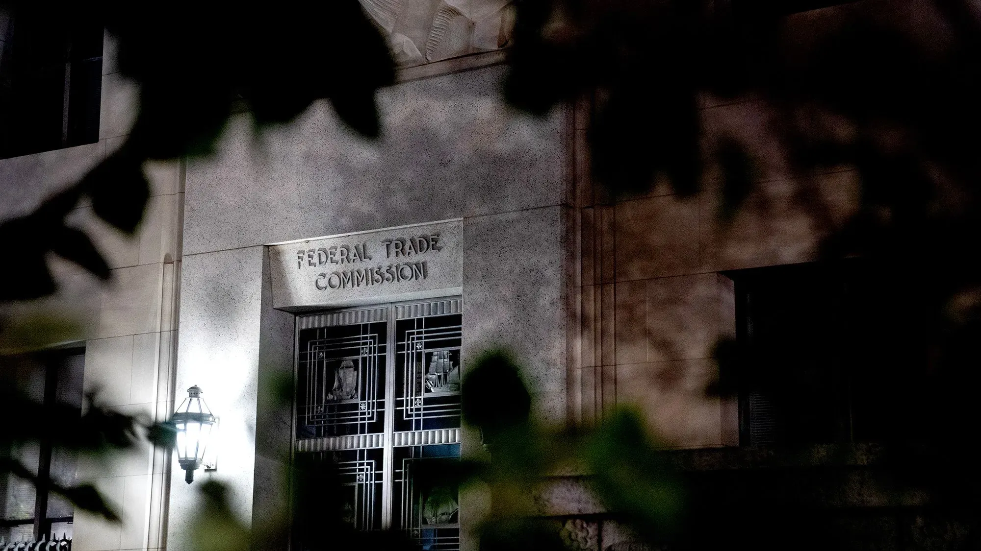 مبنى لجنة التجارة الفيدرالية الأمريكية مع إضاءة خافتة، يظهر اسم اللجنة بوضوح، محاط بأوراق الشجر، في سياق قضايا أمازون.