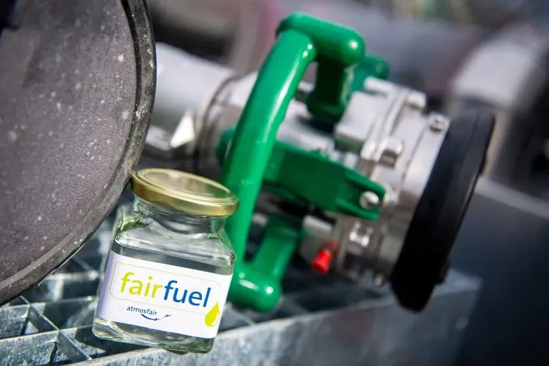 زجاجة من وقود الطيران المستدام "fairfuel" بجانب مضخة، تعكس الابتكارات في صناعة الطيران للحد من الانبعاثات الكربونية.
