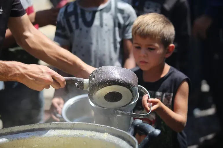 طفل صغير يحمل وعاءً أثناء توزيع الطعام في غزة، وسط مجموعة من الأطفال، في ظل الظروف الإنسانية الصعبة الناتجة عن الحرب.