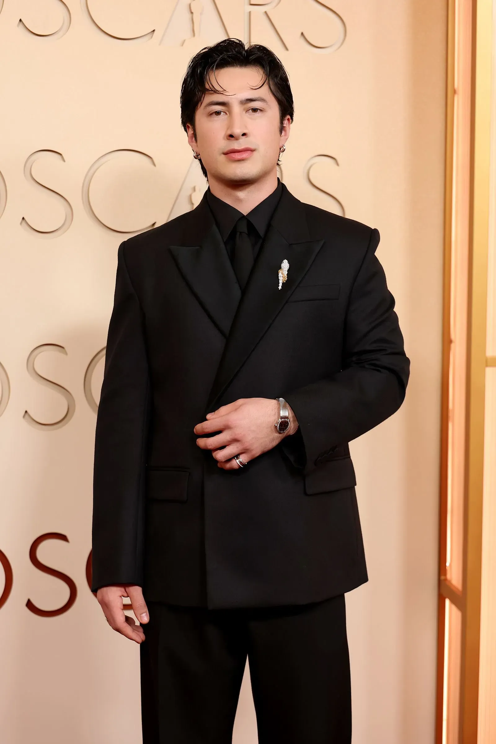 شاب يرتدي بدلة سوداء أنيقة، مع ساعة فاخرة على معصمه، في حدث رسمي. تعكس إطلالته اهتمام الجيل Z بعالم الساعات الفاخرة.