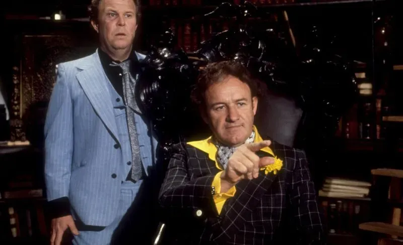 مشهد من فيلم "بوني وكلايد" يظهر جين هاكمان بدور باك بارو، مع التركيز على تعبيراته القوية وملابسه المميزة في سياق الجريمة.