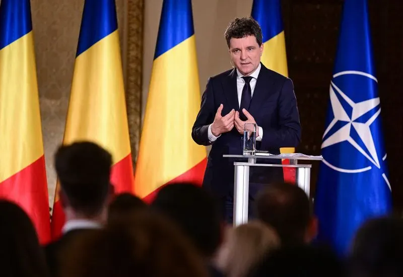 سيميون يتحدث في مؤتمر صحفي، محاطًا بأعلام رومانيا وحلف الناتو، مع التركيز على قضايا الانتخابات والتوجهات السياسية.