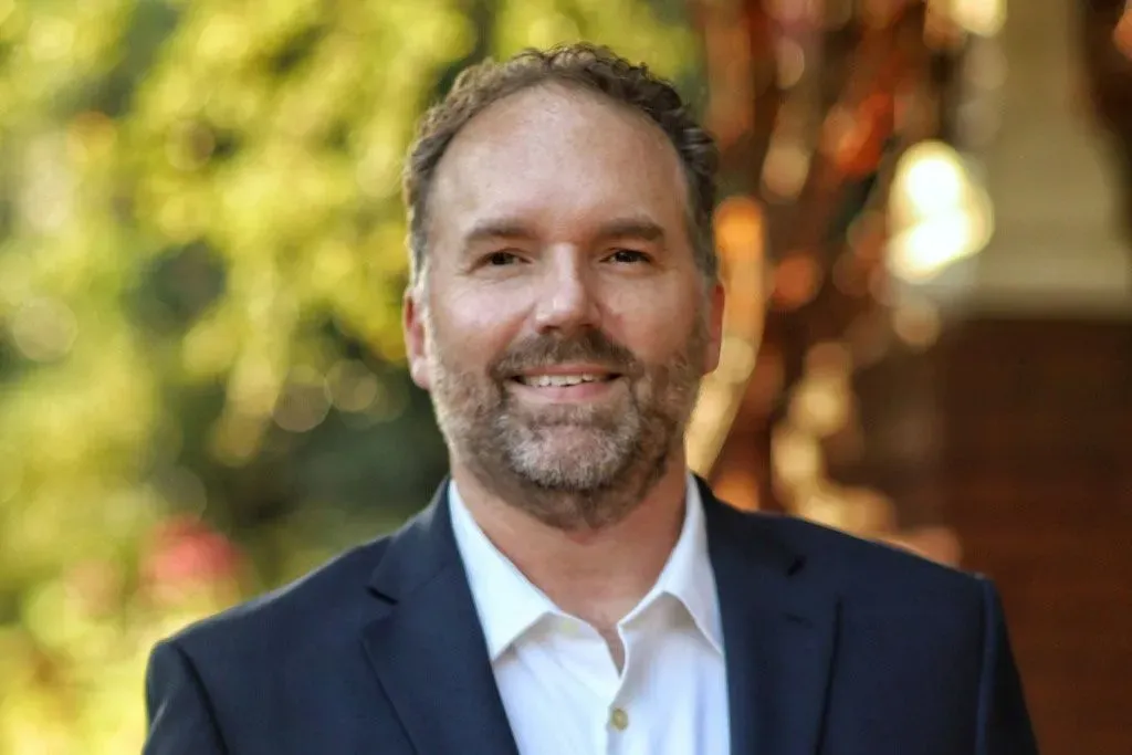 إريك جيسلر، مرشح ديمقراطي لمجلس النواب في ولاية جورجيا، مبتسم في صورة رسمية، مع خلفية طبيعية خضراء.