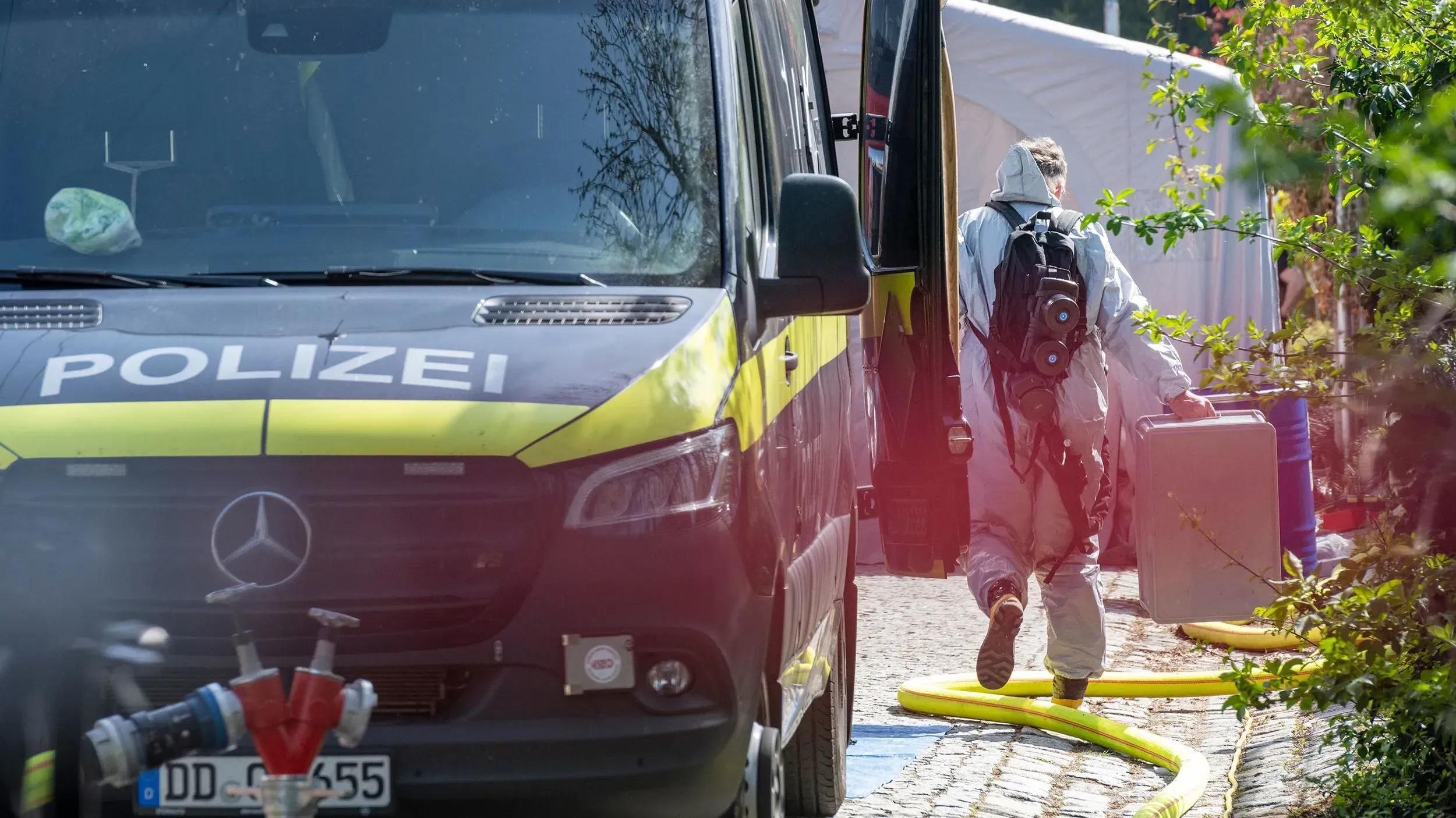 شرطة ساكسونيا تقوم بتفتيش منزل مراهق مشتبه به في صنع الريسين، مع وجود ضابط يرتدي بدلة واقية يحمل حاوية.