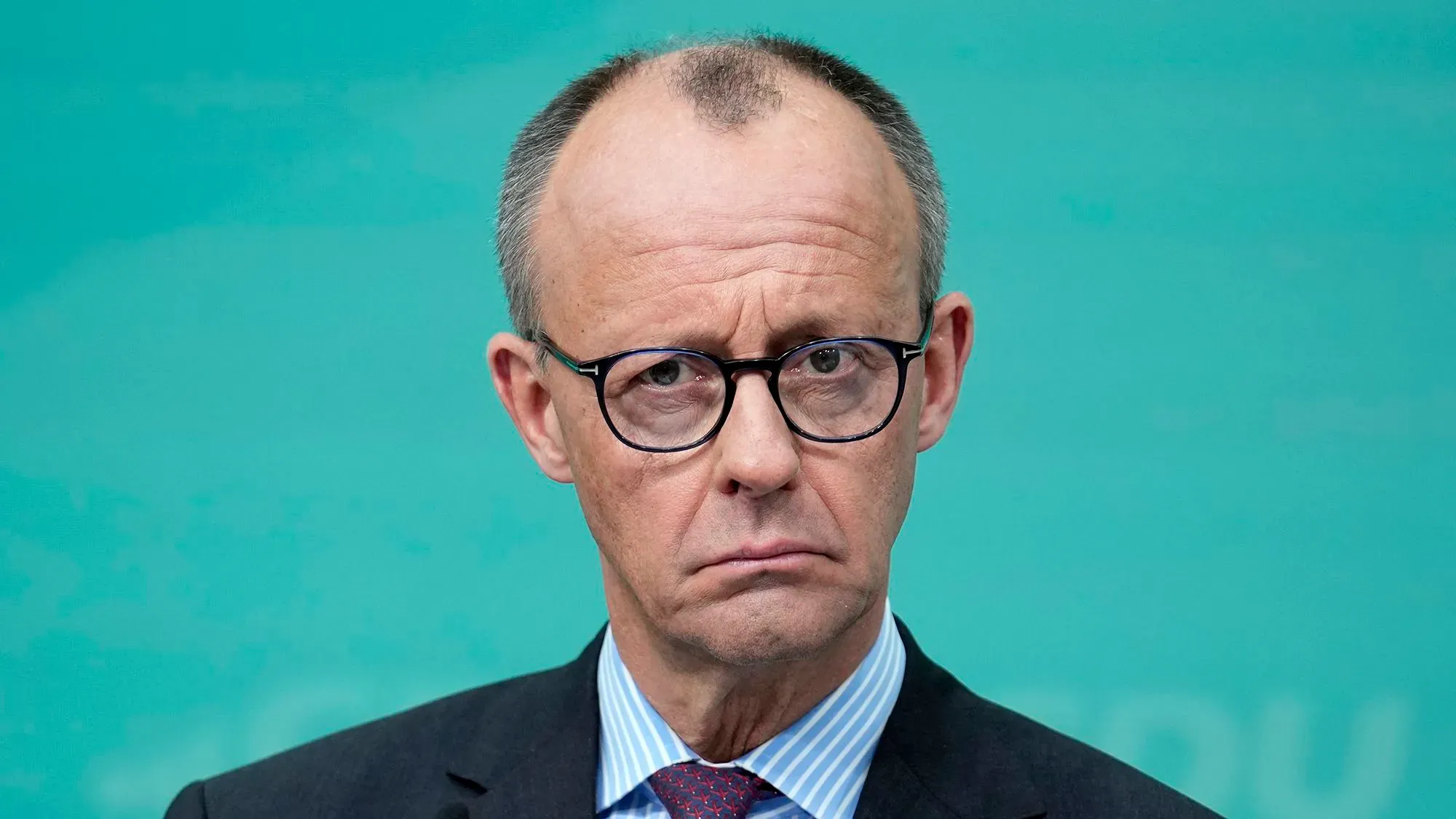 فريدريش ميرتس، زعيم حزب الاتحاد الديمقراطي المسيحي، يظهر بملامح جدية، خلفه خلفية زرقاء، في سياق المفاوضات الائتلافية في ألمانيا.