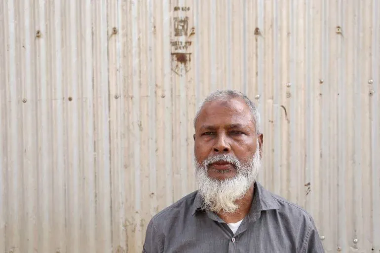 رجل مسن ذو لحية بيضاء يقف أمام جدار معدني، يعبر عن قلقه بشأن تأثير إعادة رسم الحدود الانتخابية على المسلمين في آسام.
