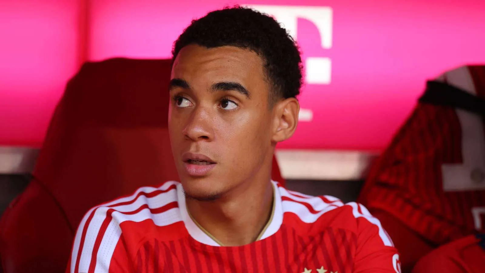 جمال موسيالا لاعب بايرن ميونخ الشاب يجلس على مقاعد البدلاء مرتدياً زي الفريق الأحمر، يعكس تحدياته الصحية ونوبات الغياب العصبية المؤقتة.