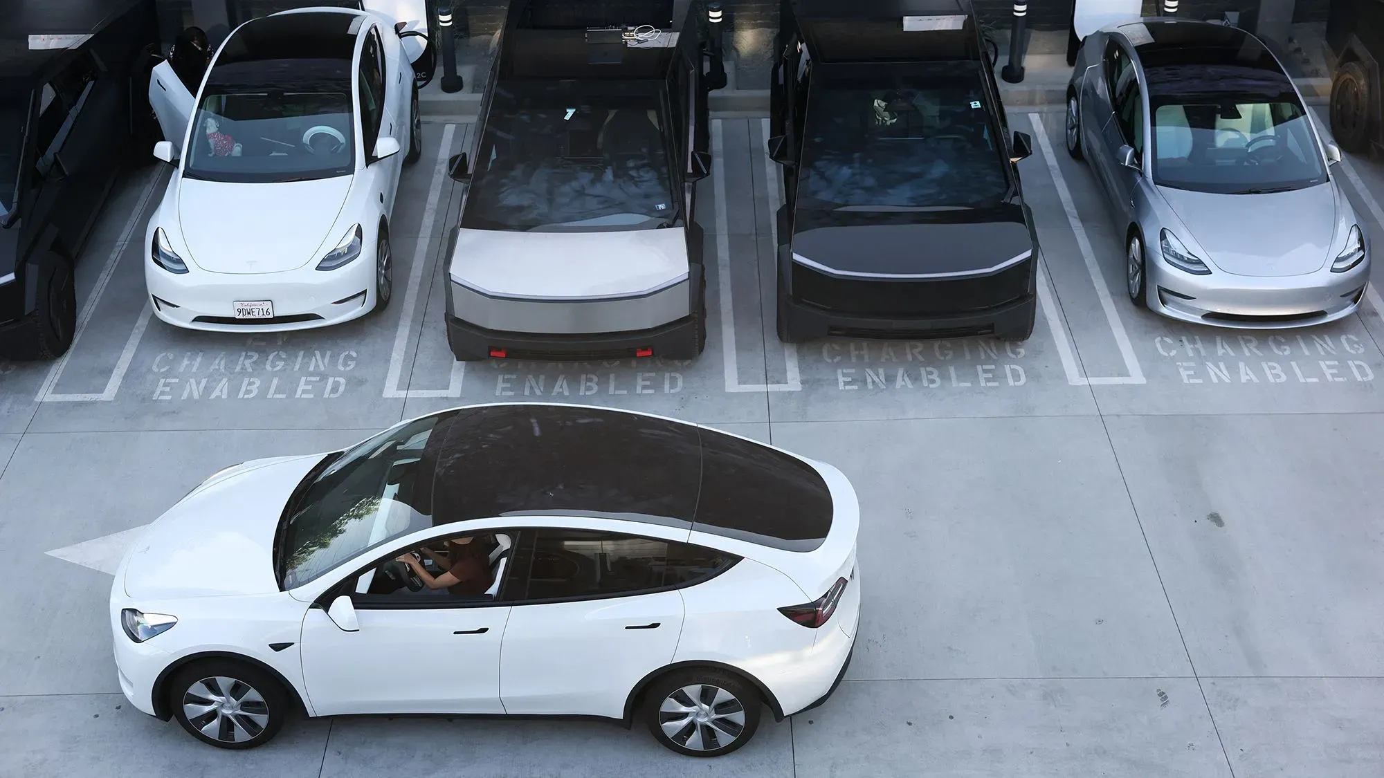 سيارة تسلا بيضاء متوقفة في موقف سيارات مخصص للشحن، مع سيارات كهربائية أخرى، تعكس التحديات التي تواجه تسلا في ظل انخفاض المبيعات.