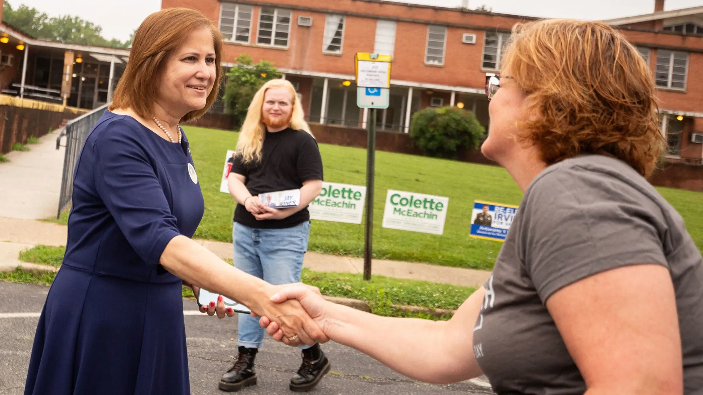 غزالة هاشمي، المرشحة الديمقراطية لمنصب نائب حاكم فيرجينيا، تتصافح مع ناخبة خلال حملة انتخابية، مع وجود لافتات خلفية.