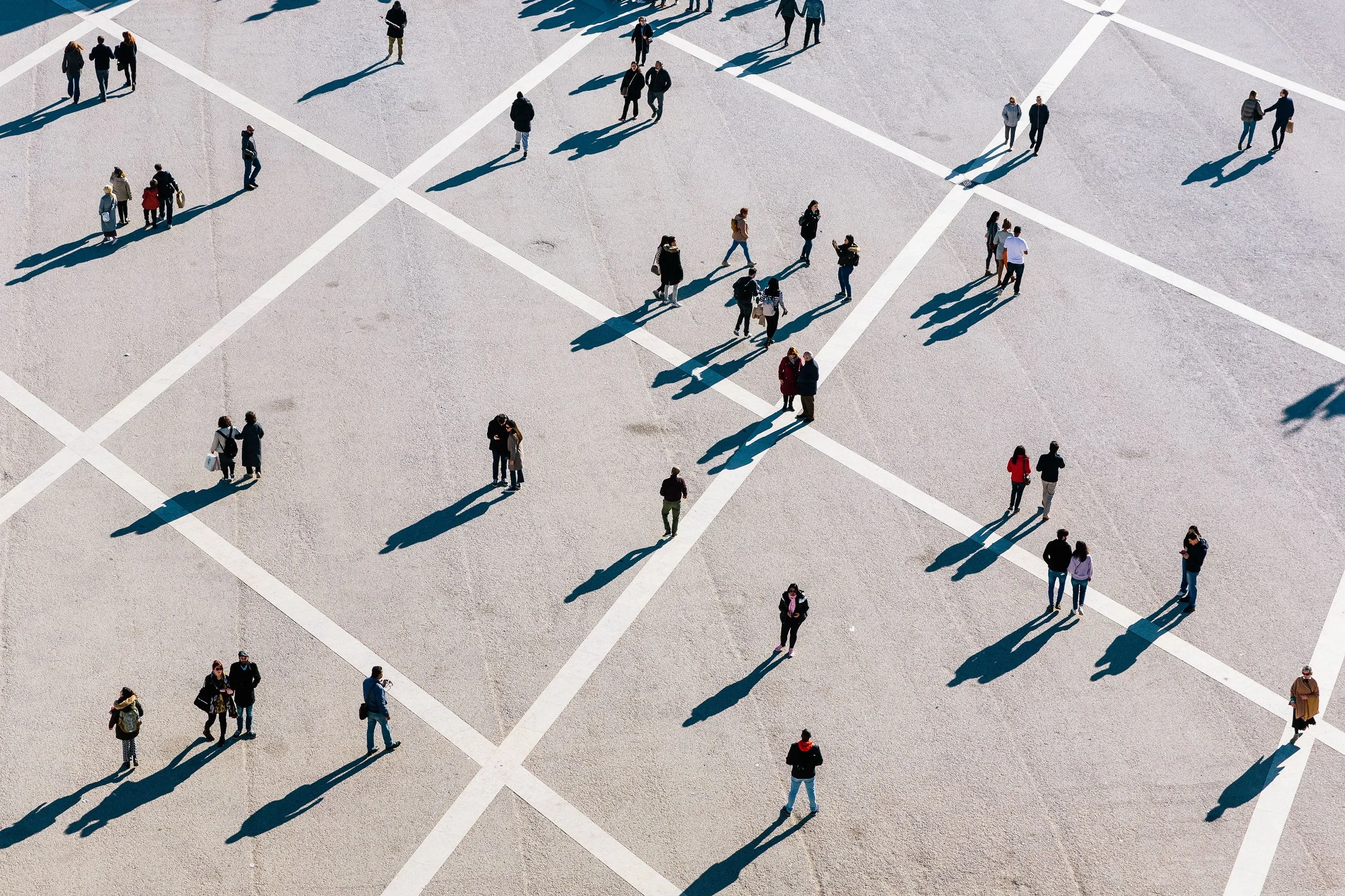 صورة تظهر مجموعة من الأشخاص يتجولون في ساحة مفتوحة، مع ظلالهم الممتدة على الأرض. تعكس الصورة التغيرات في معدلات الوفيات والصحة العامة.