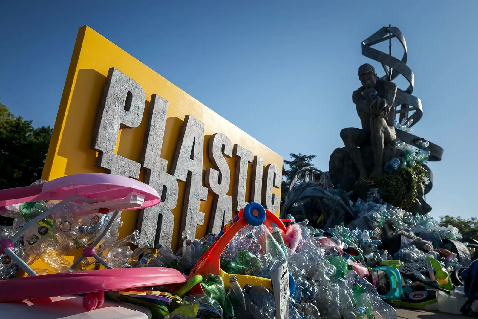 تمثال يُظهر شخصًا يجلس بجوار لافتة كبيرة مكتوب عليها "حرروا البلاستيك"، محاطًا بالنفايات البلاستيكية، مما يعكس أزمة التلوث البلاستيكي العالمية.