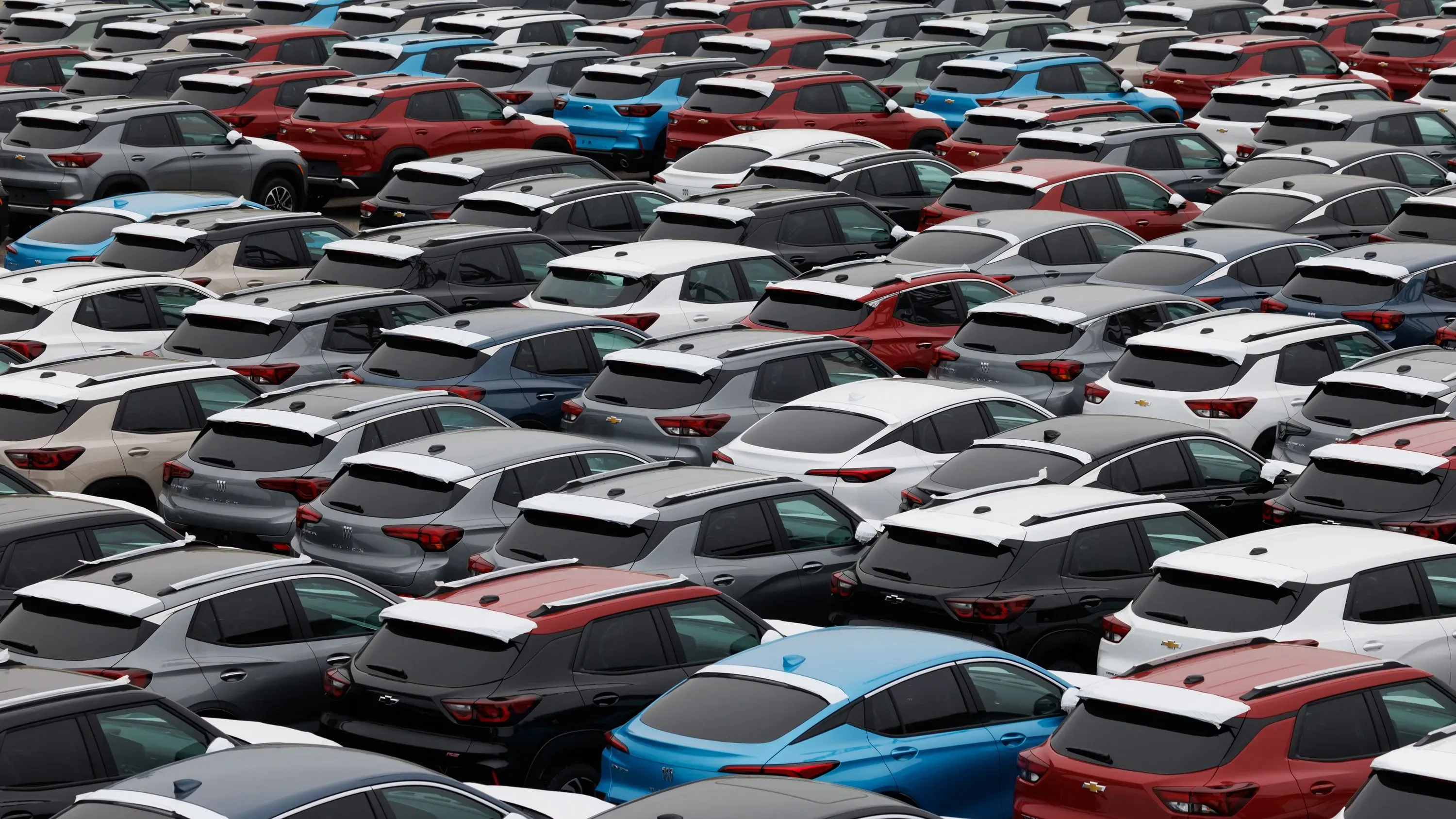 مصفوفة من السيارات الجديدة المتنوعة الألوان، تشمل سيارات من جنرال موتورز، في ساحة تجميع، تعكس استثمار الشركة في الإنتاج المحلي.