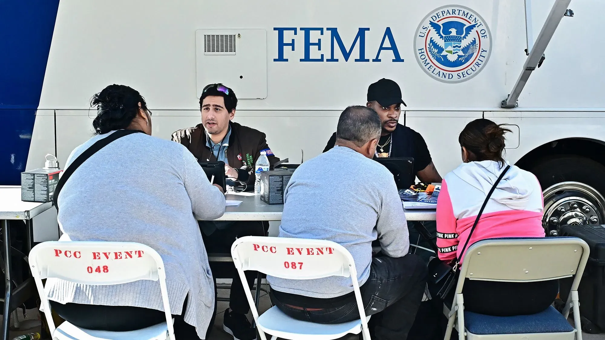 تظهر الصورة مجموعة من الأشخاص يجلسون حول طاولة في موقع وكالة إدارة الطوارئ الفيدرالية (FEMA) حيث يتلقون الدعم بعد حرائق الغابات في كاليفورنيا.