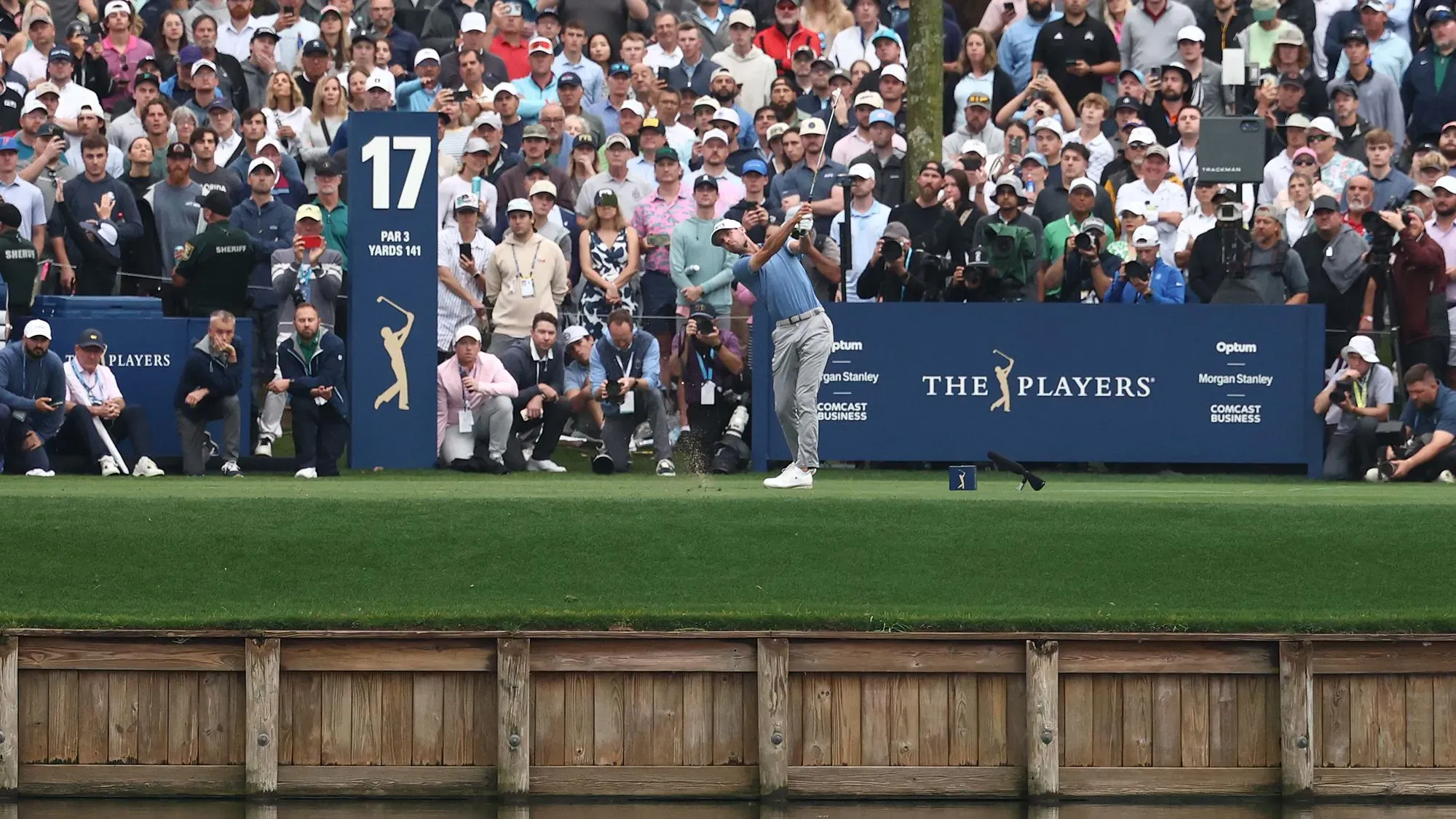 تظهر الصورة أليكس سمالي يسدد كرة الغولف في الحفرة 17 الشهيرة في TPC Sawgrass، محاطًا بجمهور متحمس.