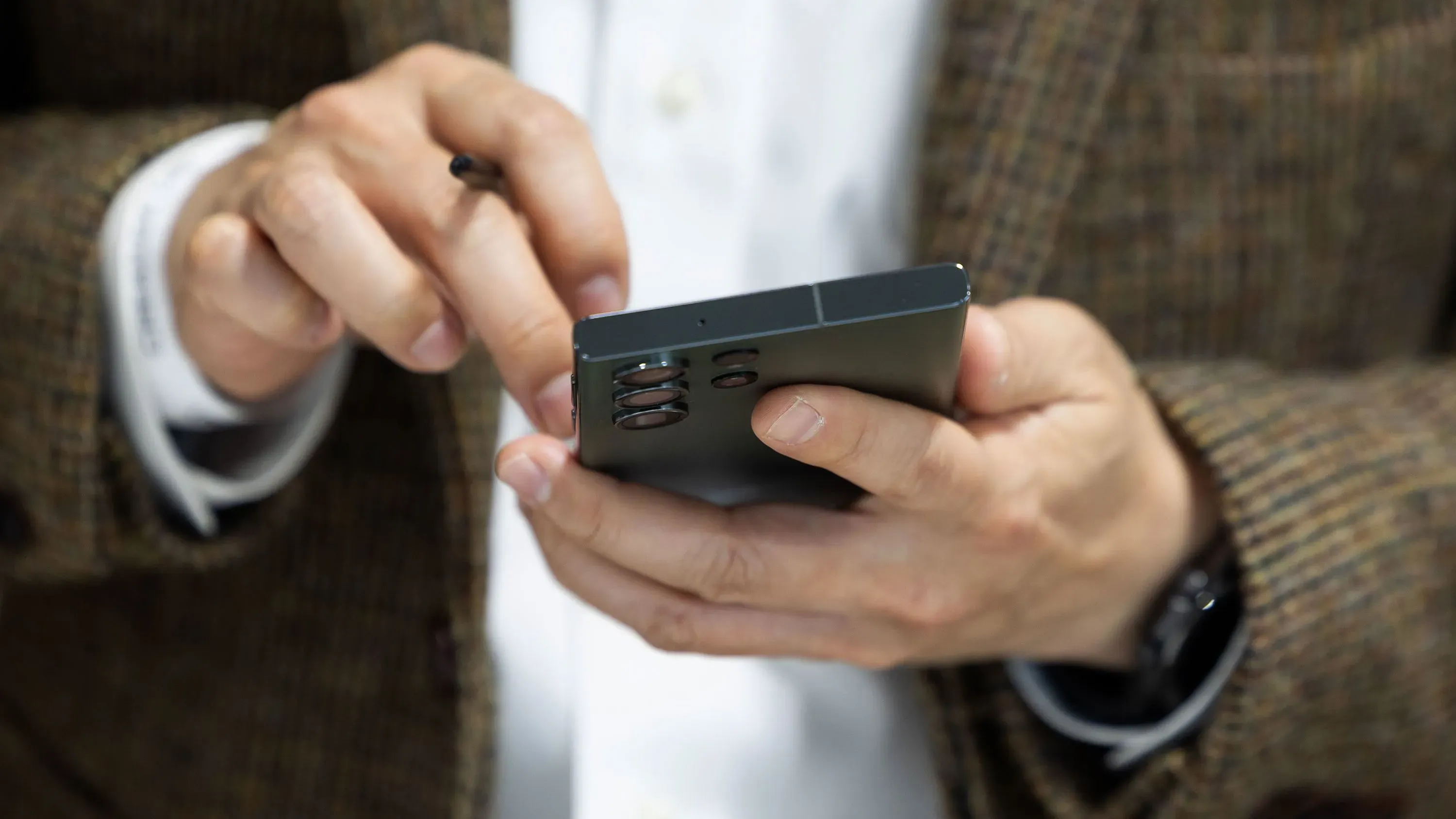 رجل يرتدي بدلة يحمل هاتفًا ذكيًا، مستخدمًا تطبيق رسائل جوجل للكشف عن الرسائل النصية الاحتيالية المتعلقة برسوم المرور.