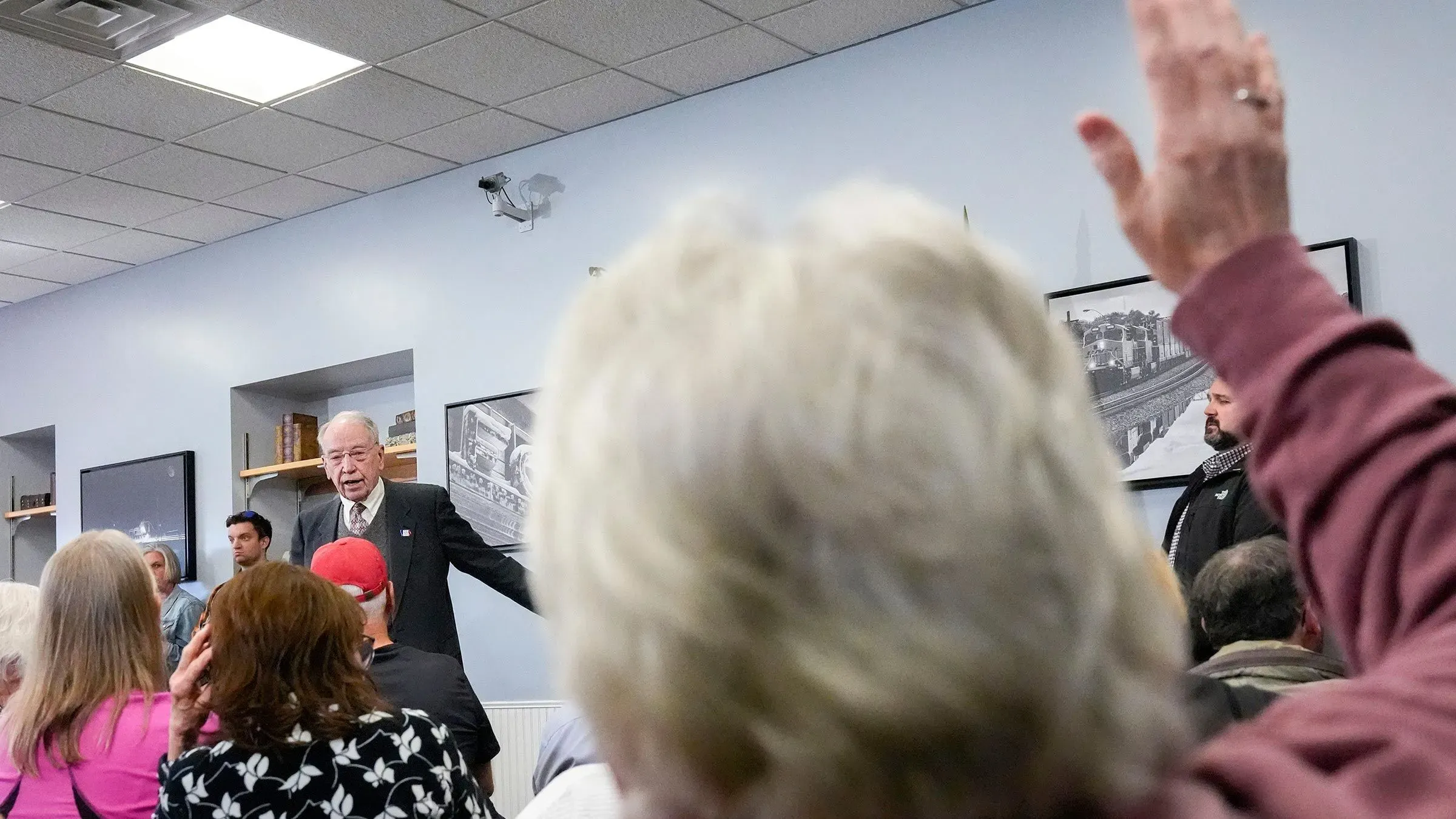 اجتماع حاشد في قاعة بلدية أيوا، حيث يطرح الحضور أسئلة على السيناتور تشاك غراسلي حول قضايا سياسية ملحة، مع رفع يد أحد الحضور.