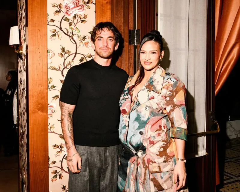 أليكس فاين وكاسي فينتورا يقفان معًا في حدث، حيث تظهر كاسي في فستان مزخرف وتبدو حاملًا. تعكس الصورة دعمهما المتبادل في مواجهة التحديات.