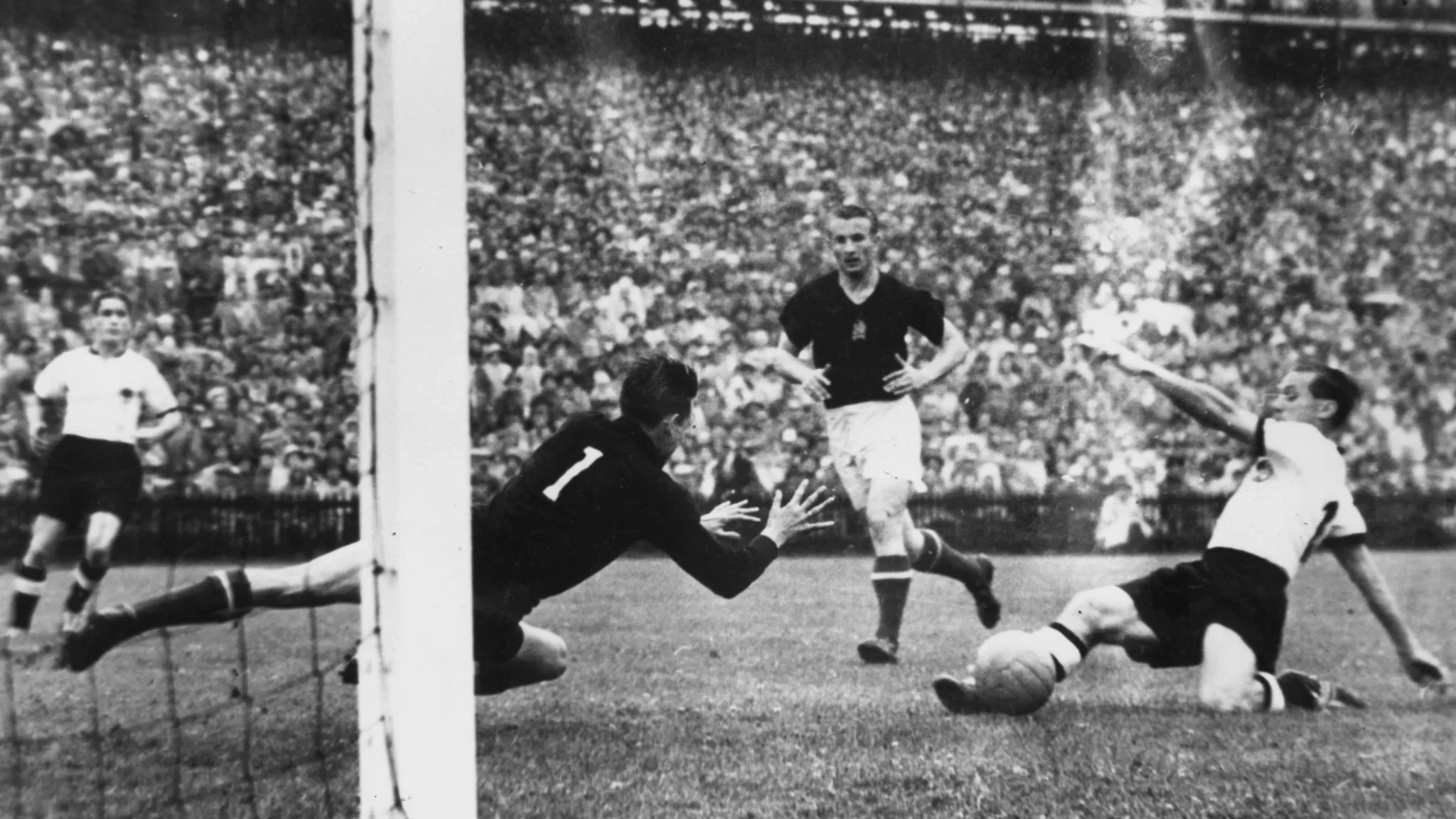 مهاجم ألماني يسدد الكرة نحو المرمى في مباراة تاريخية بكأس العالم 1954 وسط حضور جماهيري كبير.