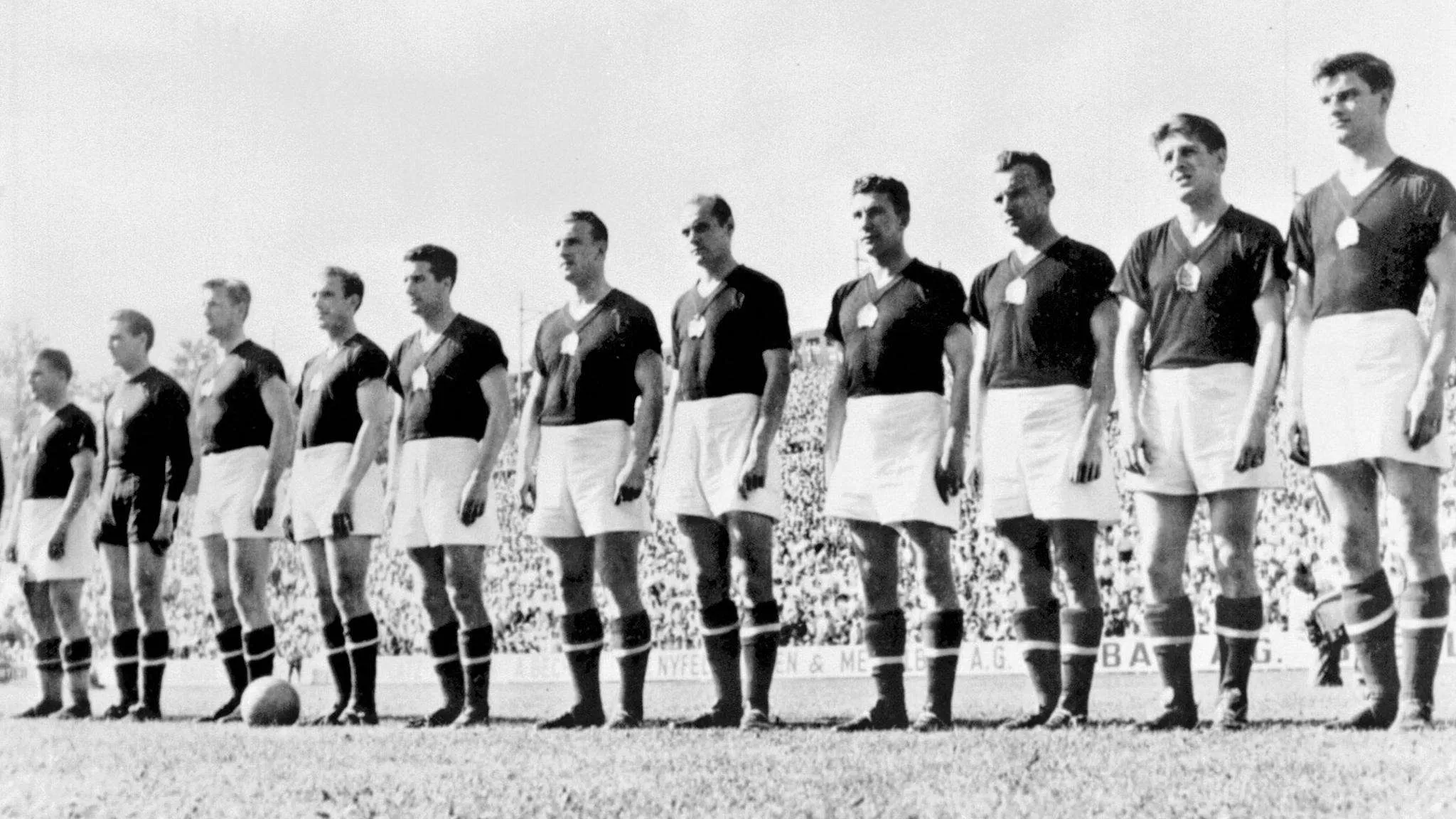 فريق كرة القدم الألماني الغربي عام 1954 يقف في صف أمام الملعب، يرتدي زيًا موحدًا باللونين الأسود والأبيض، ضمن أفضل خطوط الهجوم في تاريخ كأس العالم.