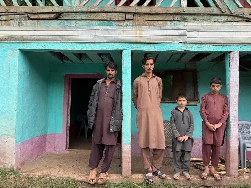 رجل و3 أطفال يقفون أمام منزل ملون في قرية سارجيوار بكشمير، يعكسون حياة المزارعين في منطقة النزاع.