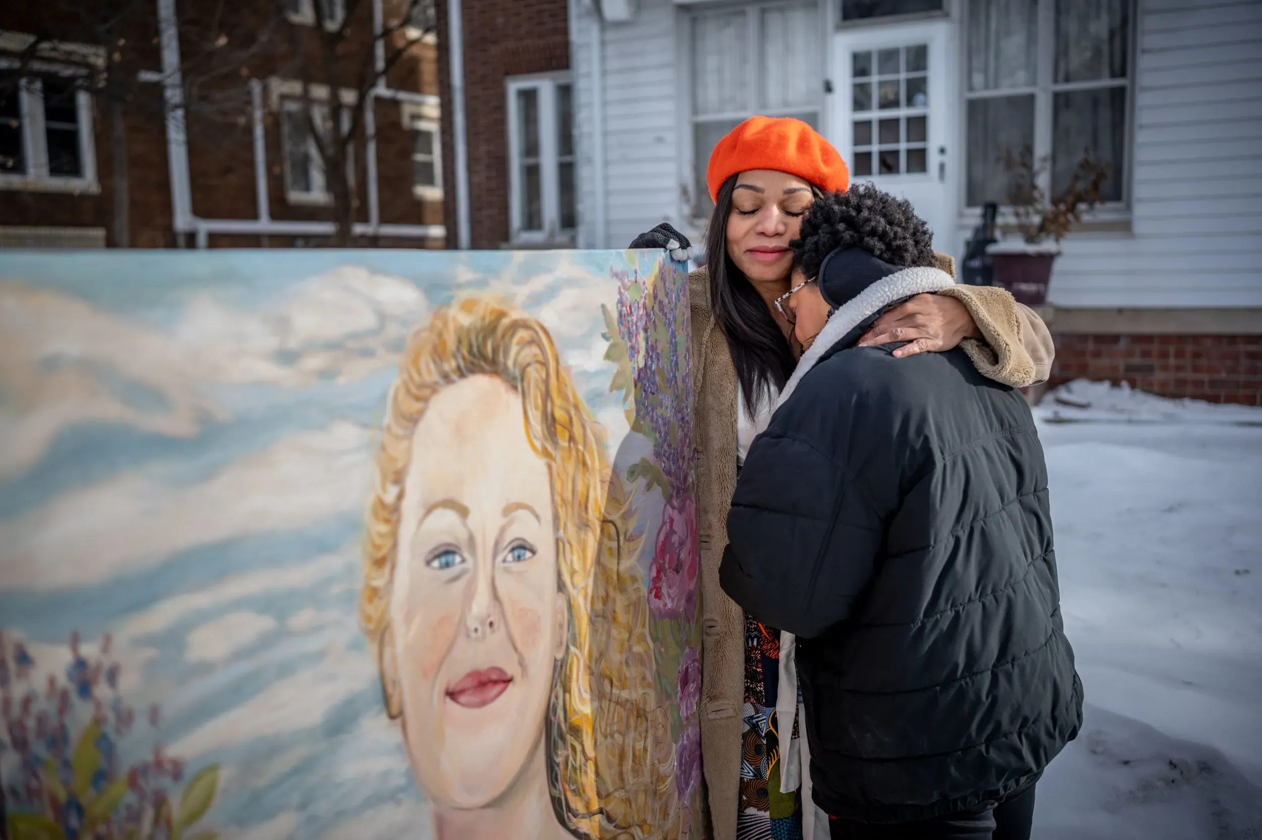 امرأة تحتضن طفلاً بجانب لوحة تذكارية لرينيه نيكول جود، مع خلفية ثلجية تعكس أجواء الشتاء في مينيابوليس.