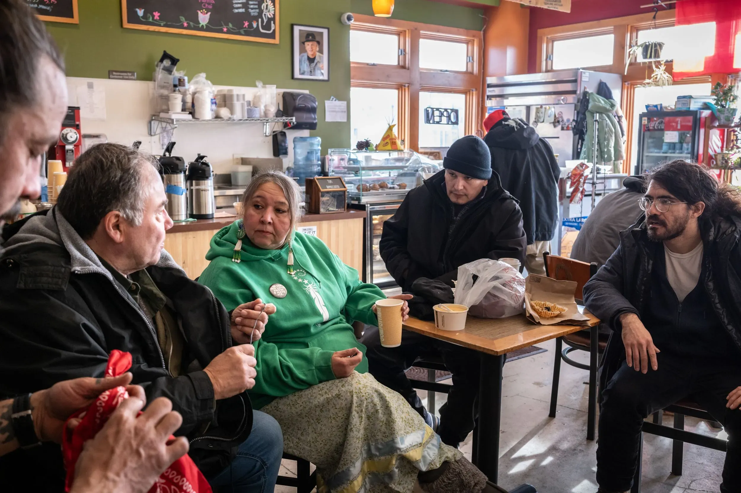 مجموعة من الأشخاص يجلسون في مقهى، يتبادلون الحديث بينما يحتسون المشروبات. تعكس الأجواء روح المجتمع والدعم في أوقات الأزمات.