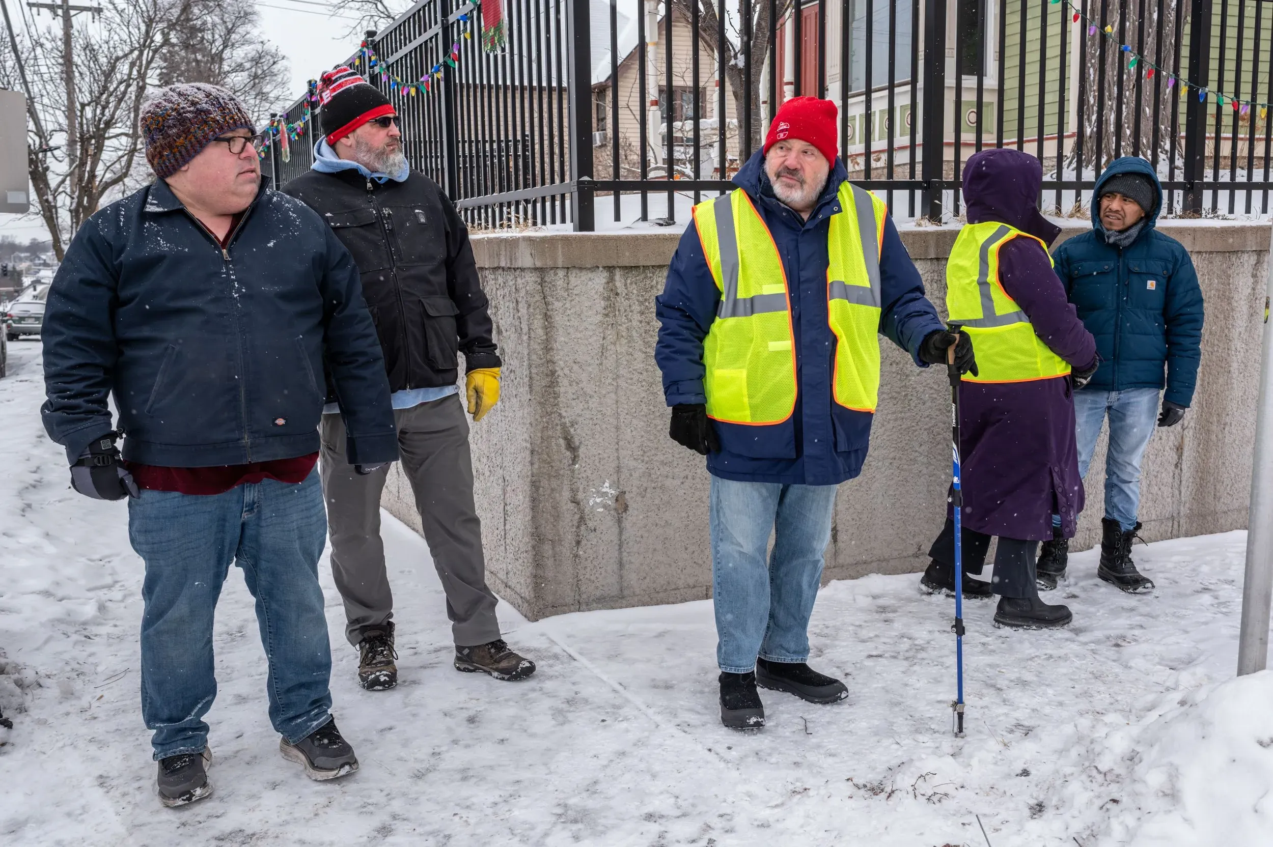 مجموعة من الأشخاص يرتدون سترات عاكسة، يقفون في الثلج ويتحدثون معًا، يعكسون روح التضامن في أوقات الأزمات في مينيابوليس.