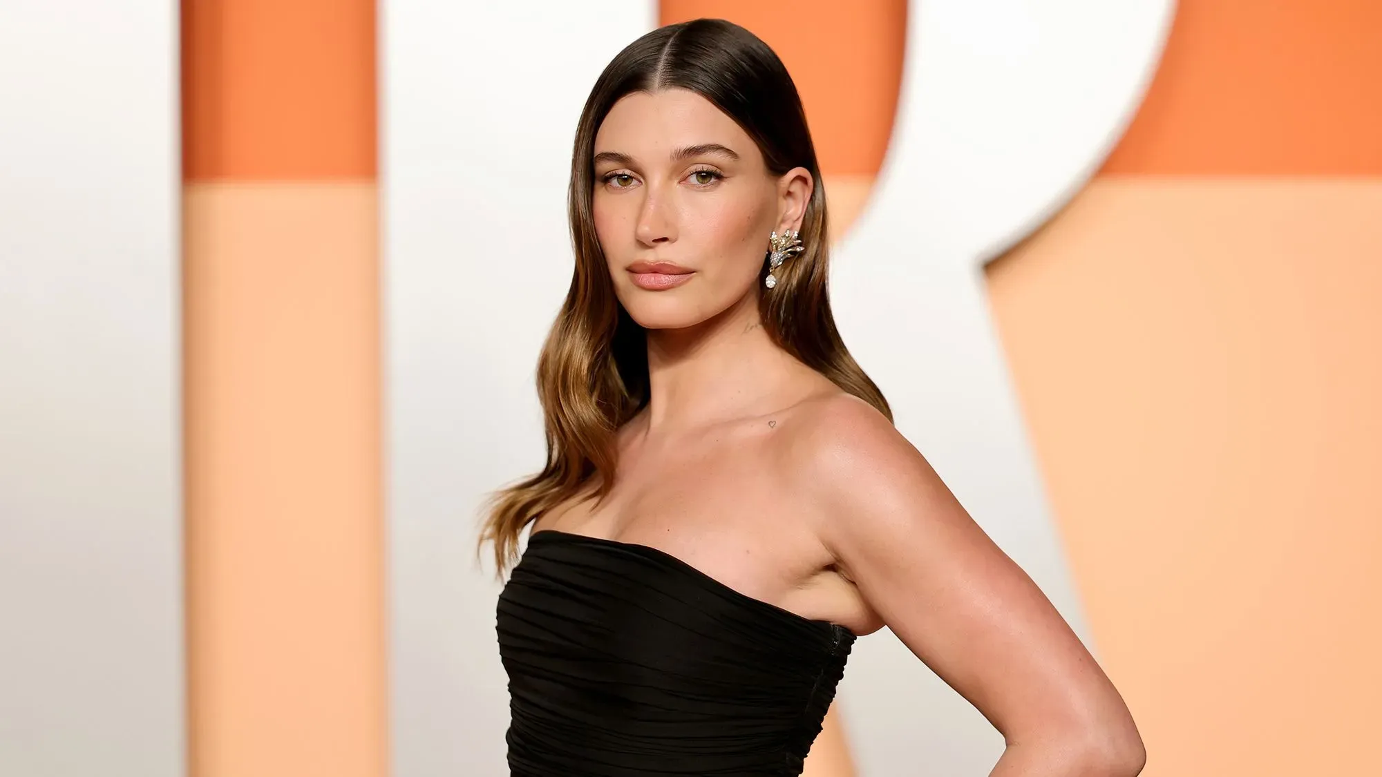 هايلي بيبر تتحدث عن تجربتها مع كيسات المبيض، مرتدية فستان أسود أنيق، وتظهر تعبيرات وجهها الجادة في حدث عام.