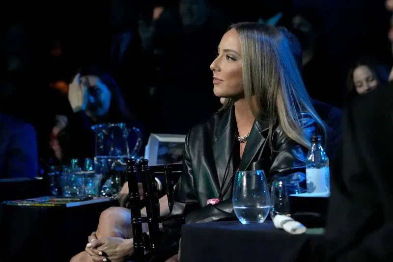 هايلي جيد، ابنة إيمينيم، تجلس في حدث، تحمل نظرة تأملية. خلفها، تظهر أضواء خافتة وجمهور.