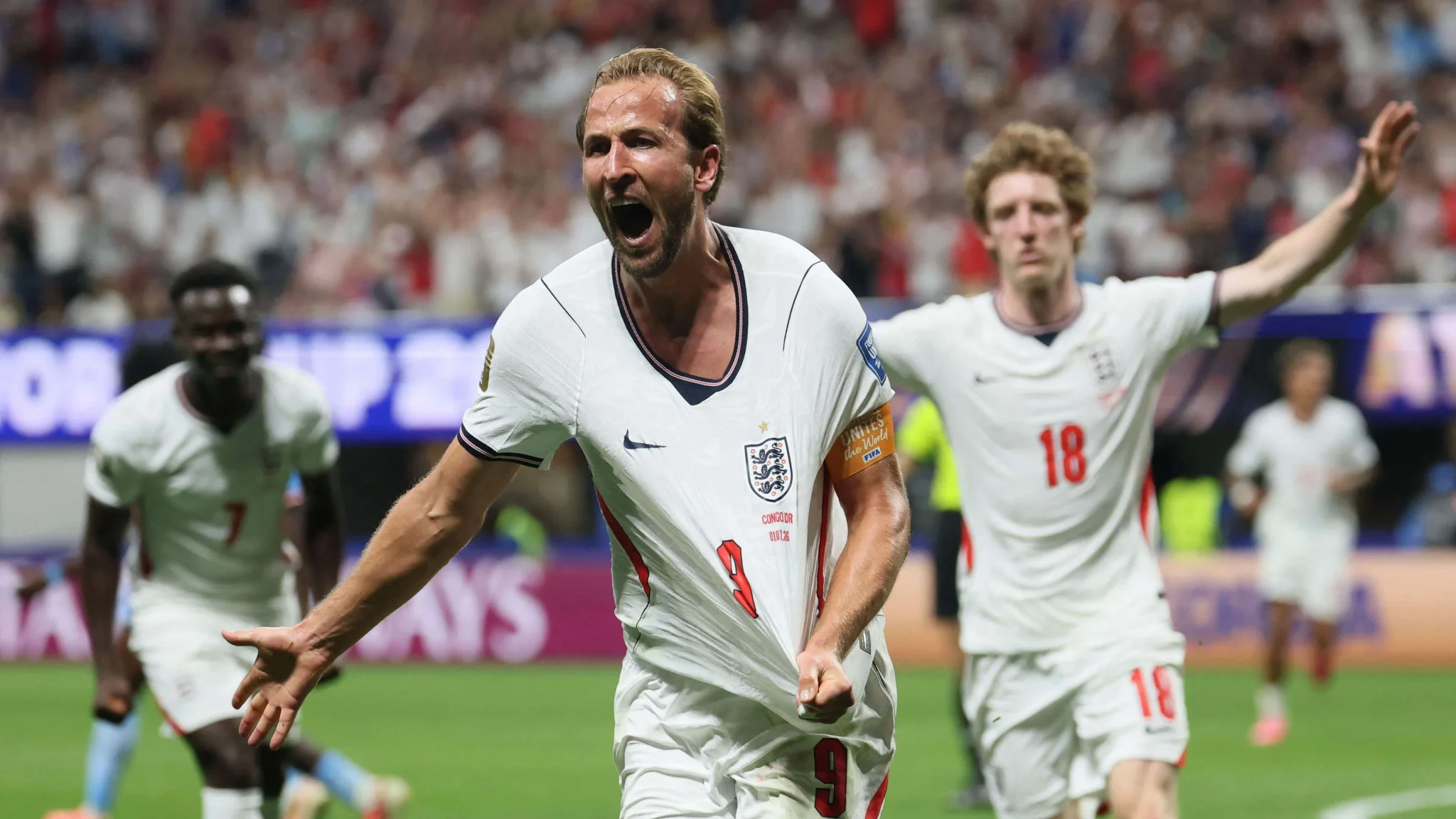 هاري كين يحتفل بهدفه الحاسم مع منتخب إنجلترا في مباراة كأس العالم، مع زملائه في الخلفية وسط أجواء حماسية في الملعب.