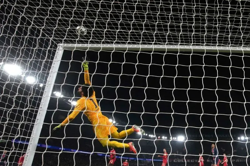 حارس مرمى ليفربول، أليسون، يقفز لصد كرة عالية خلال مباراة دوري أبطال أوروبا، مع إضاءة الملعب الساطعة خلفه.