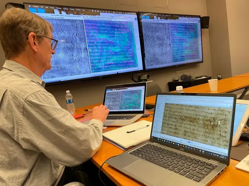 باحث يستخدم أجهزة كمبيوتر لمراجعة وثيقة الماغنا كارتا الأصلية في كلية الحقوق بجامعة هارفارد، مع شاشات تعرض التحليلات الرقمية.