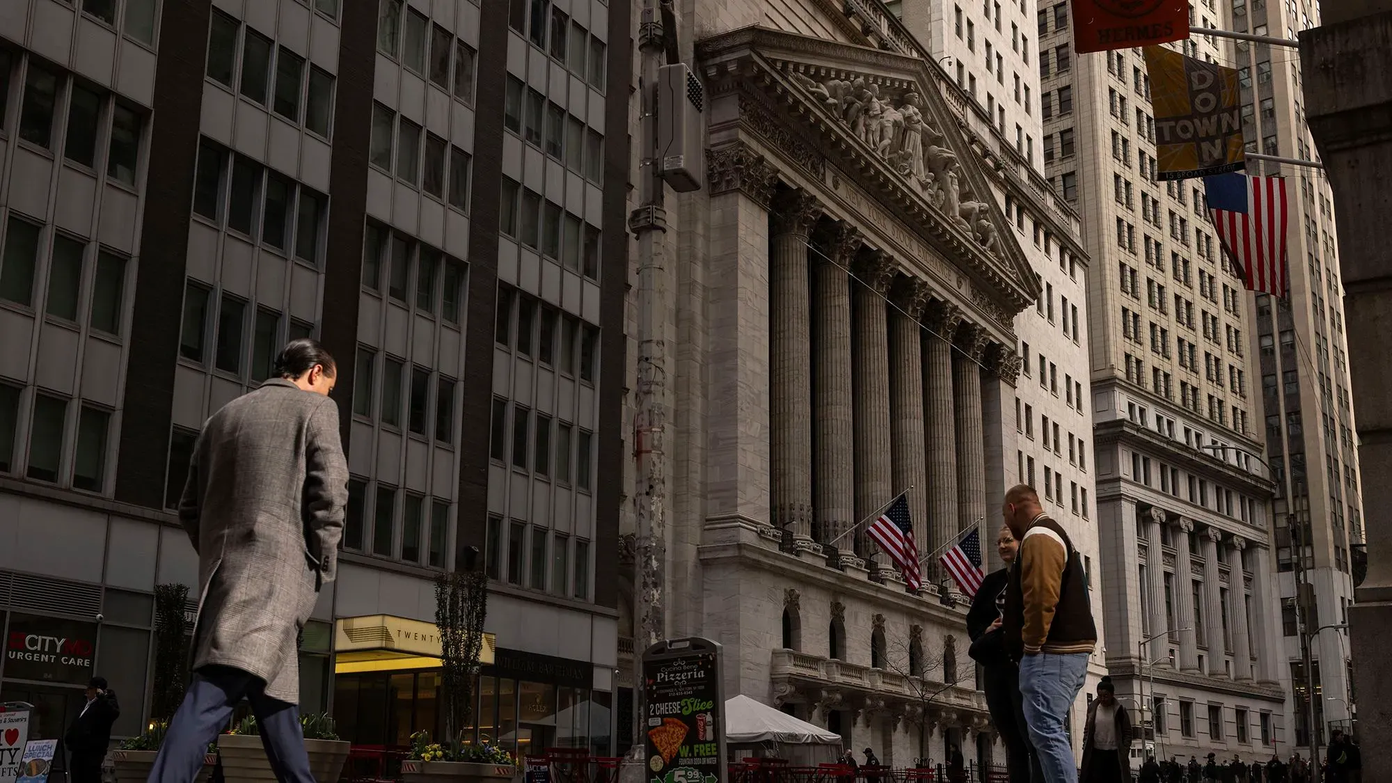 واجهة بورصة نيويورك مع متسوقين في الشارع، تعكس حالة السوق الأمريكية وتأثير الحرب التجارية على الاقتصاد.