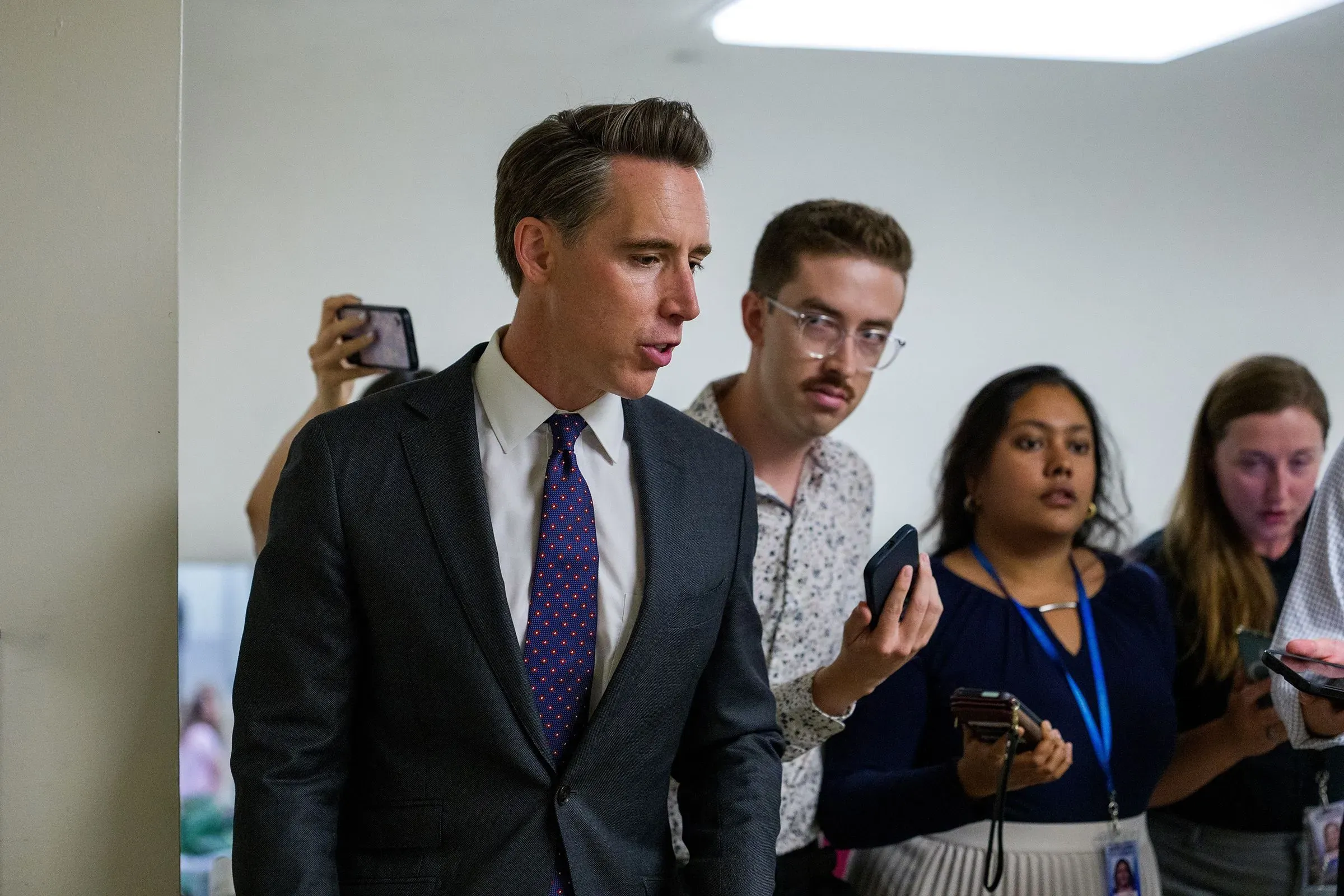 السيناتور جوش هاولي يتحدث مع الصحفيين حول مشروع قانون حظر تداول الأسهم، محاطًا بمجموعة من الصحفيين أثناء حديثه.