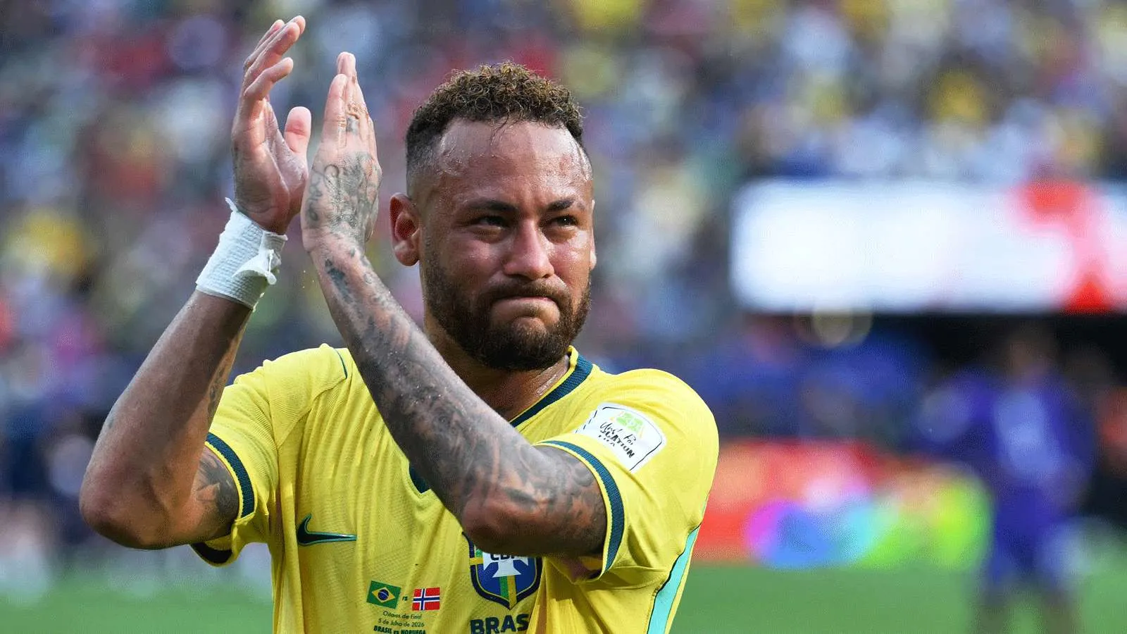 لاعب كرة قدم برازيلي يرتدي قميص منتخب البرازيل الأصفر يصفق للجمهور في ملعب مكتظ خلال مباراة دولية.