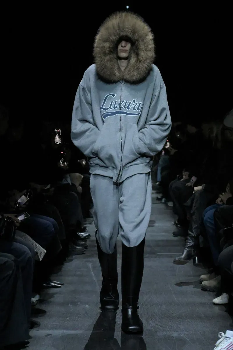 عارض أزياء يرتدي سترة رمادية كبيرة مع غطاء رأس مزود بفرو، يعكس أسلوب الموضة المعاصر في عرض أزياء حديث.