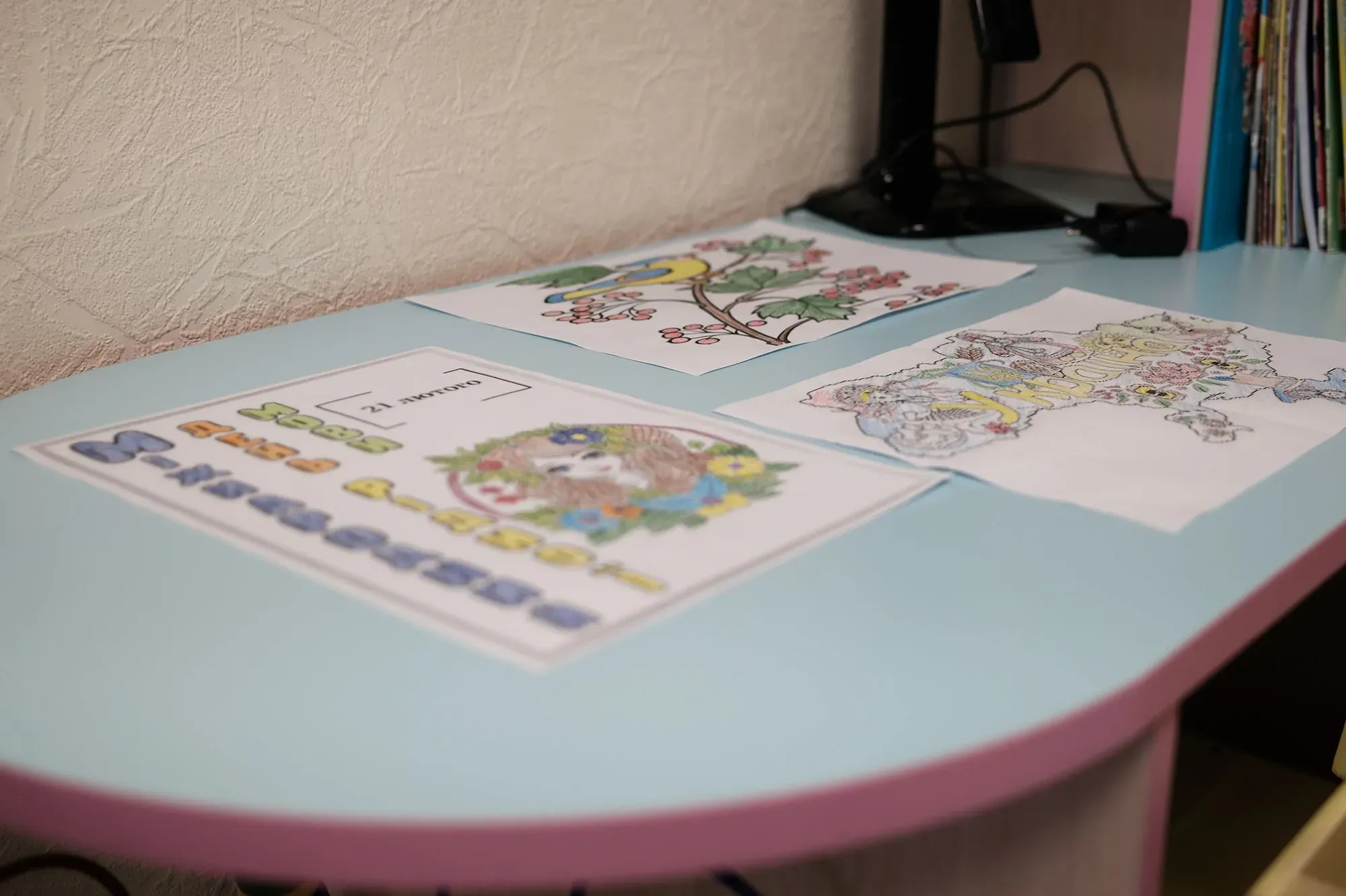 رسومات ملونة لأطفال على طاولة زرقاء، تتضمن مشاهد طبيعية وحيوانات، تعكس تأثير الحرب على الأوكرانيين واحتياجاتهم النفسية.