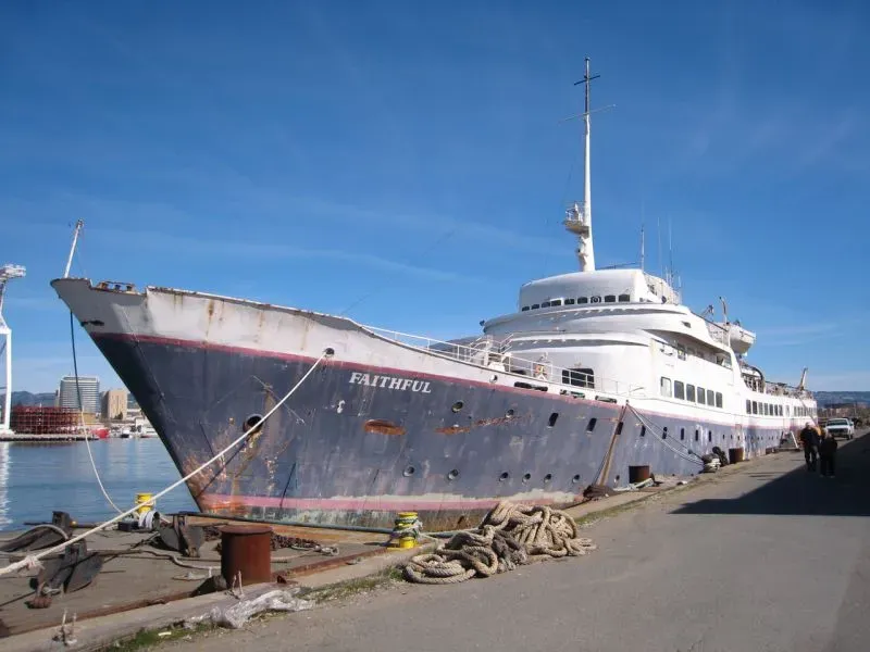 سفينة سياحية قديمة تُدعى "فايثفول"، تظهر في حالة تدهور، ترسو في ميناء تحت سماء زرقاء، تعكس تاريخها الغني.