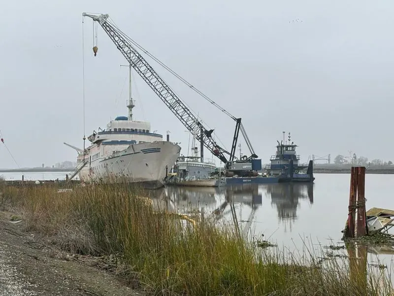 سفينة سياحية تاريخية تُعرف باسم "أورورا" تُهدم باستخدام رافعة في موقعها على الماء، مع وجود معدات أخرى في الخلفية.
