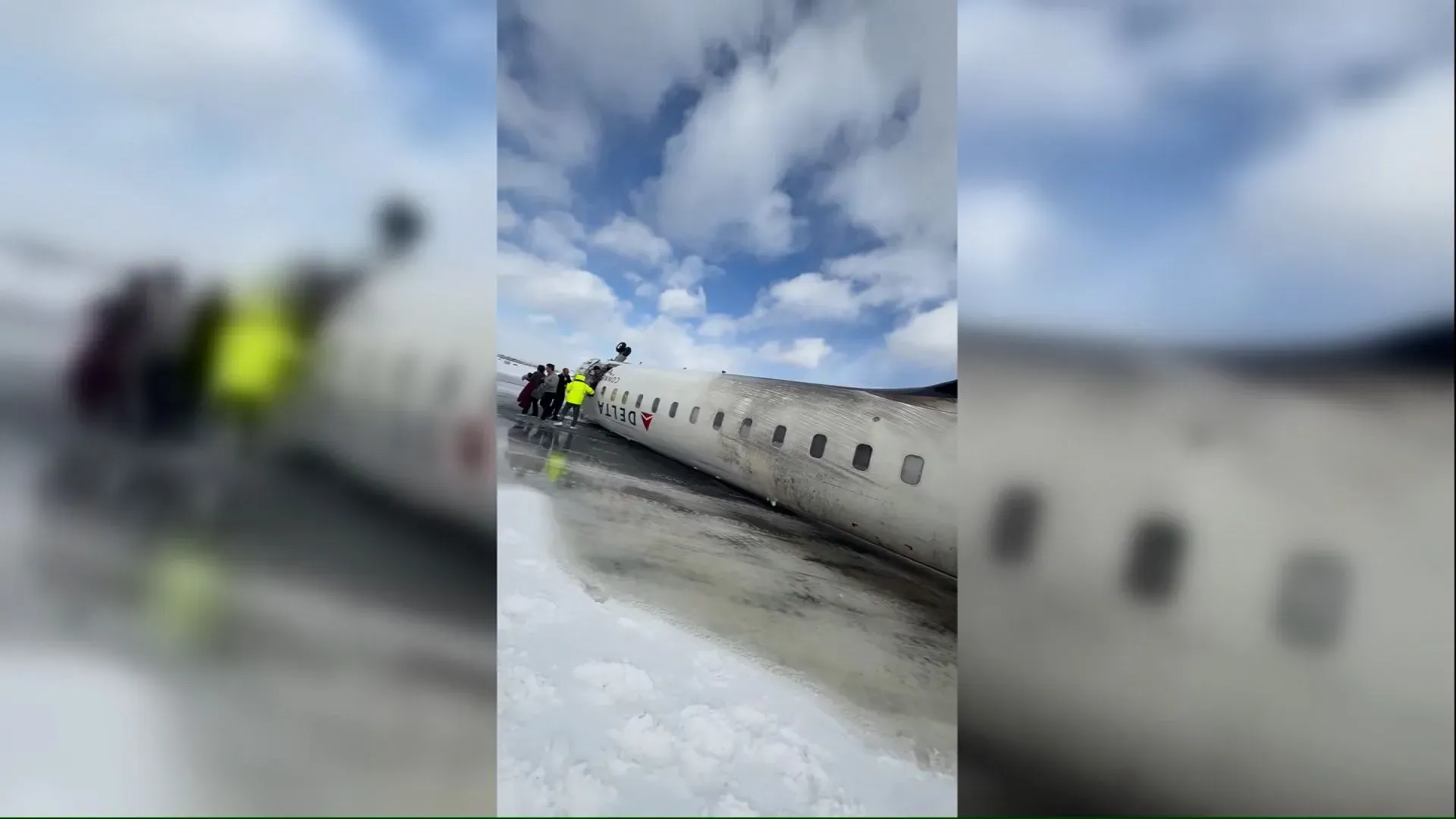 راكبون يخرجون من طائرة دلتا المقلوبة على مدرج ثلجي في تورنتو، مع وجود السماء الزرقاء والغيوم في الخلفية، بعد حادث هبوط غير متوقع.
